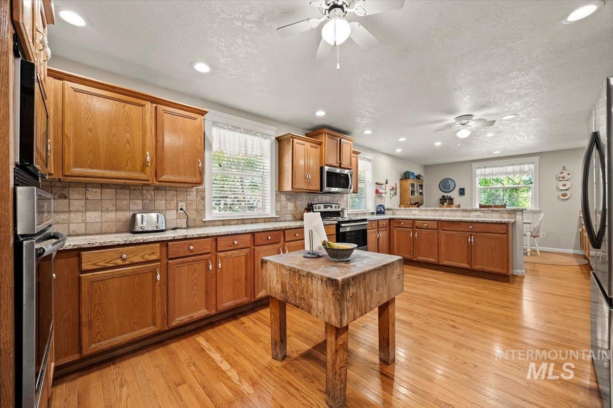 Kitchen with stainless steel appliances, a ceiling fan, a peninsula, light wood-style floors, and brown cabinets