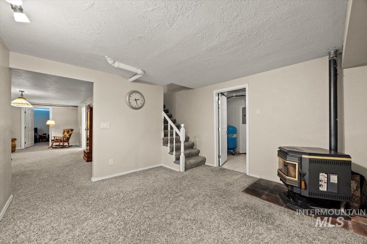 Living area with a wood stove, stairs, carpet flooring, and a textured ceiling