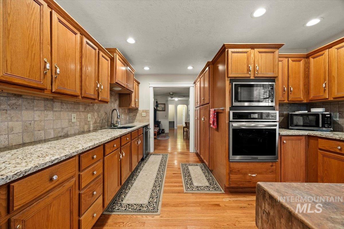 Kitchen featuring stainless steel appliances, brown cabinets, light wood-style floors, backsplash, and recessed lighting