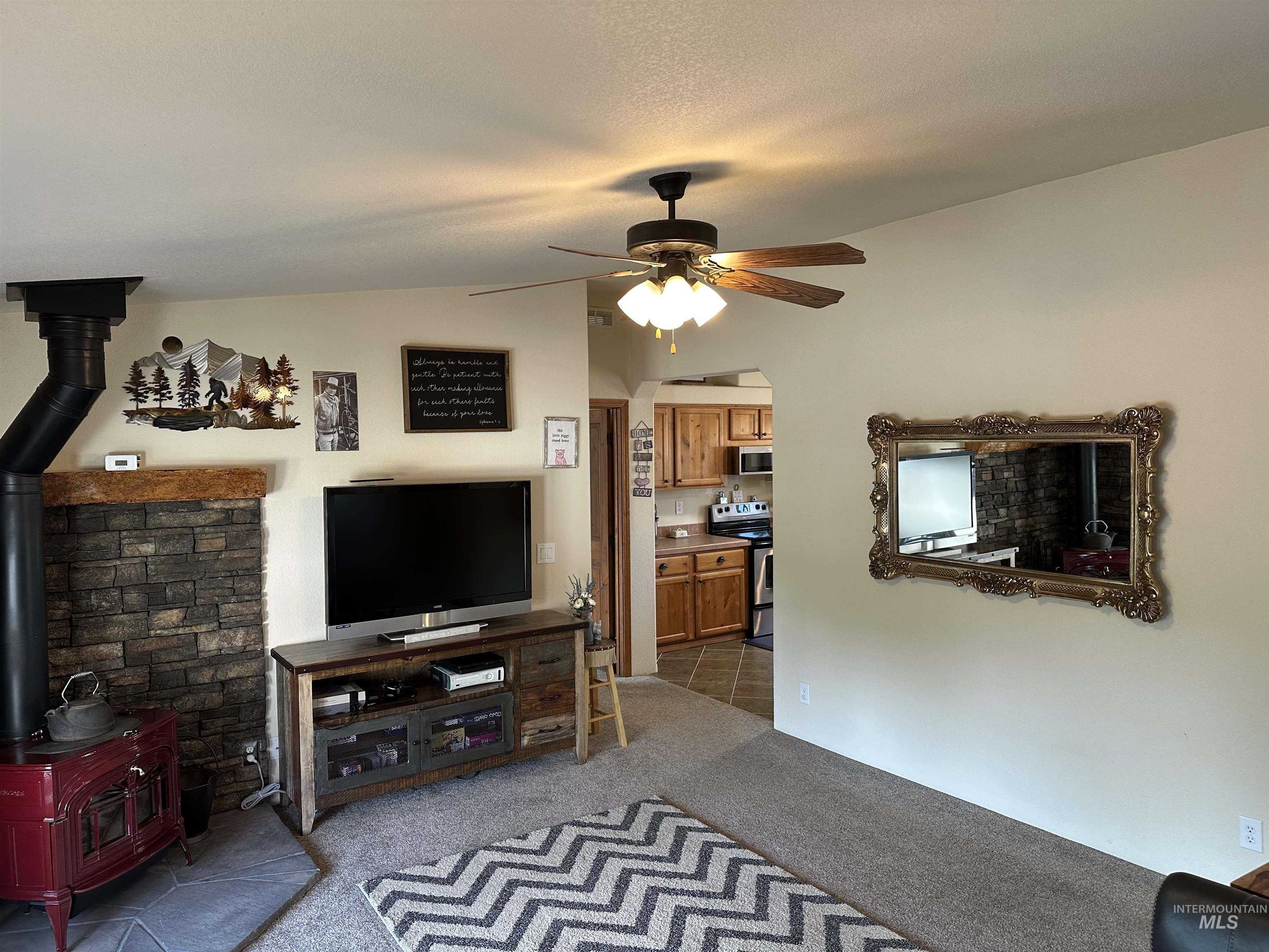 Living area with a wood stove, light colored carpet, vaulted ceiling, and a ceiling fan