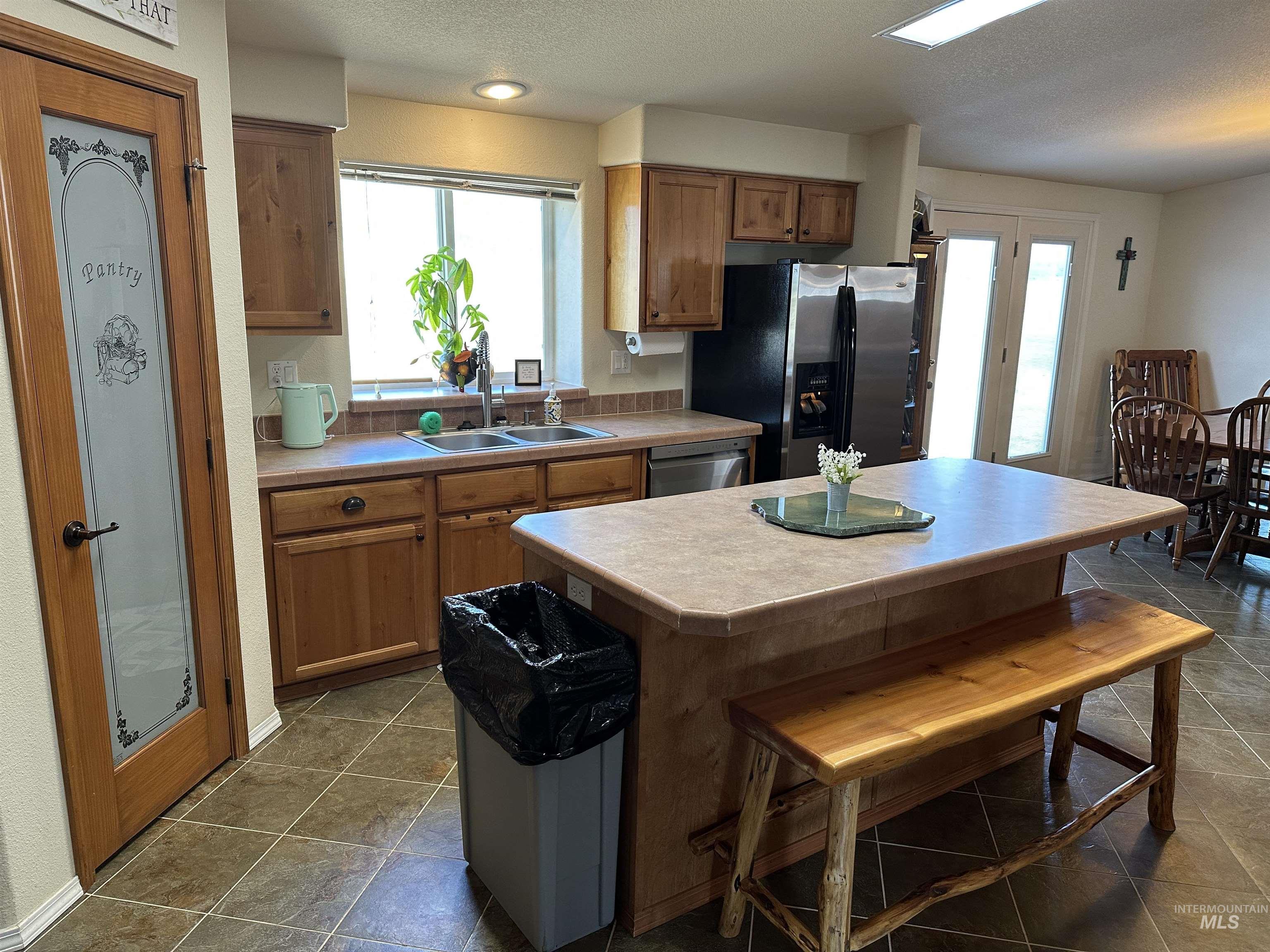 Kitchen with brown cabinets, light countertops, a textured ceiling, a center island, and appliances with stainless steel finishes