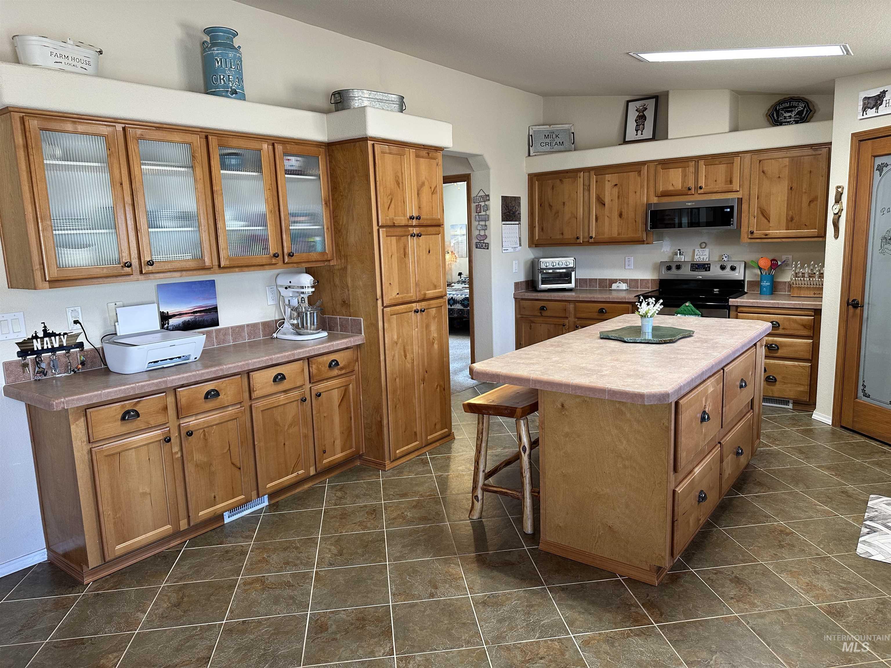 Kitchen with appliances with stainless steel finishes, glass insert cabinets, a center island, vaulted ceiling, and brown cabinets