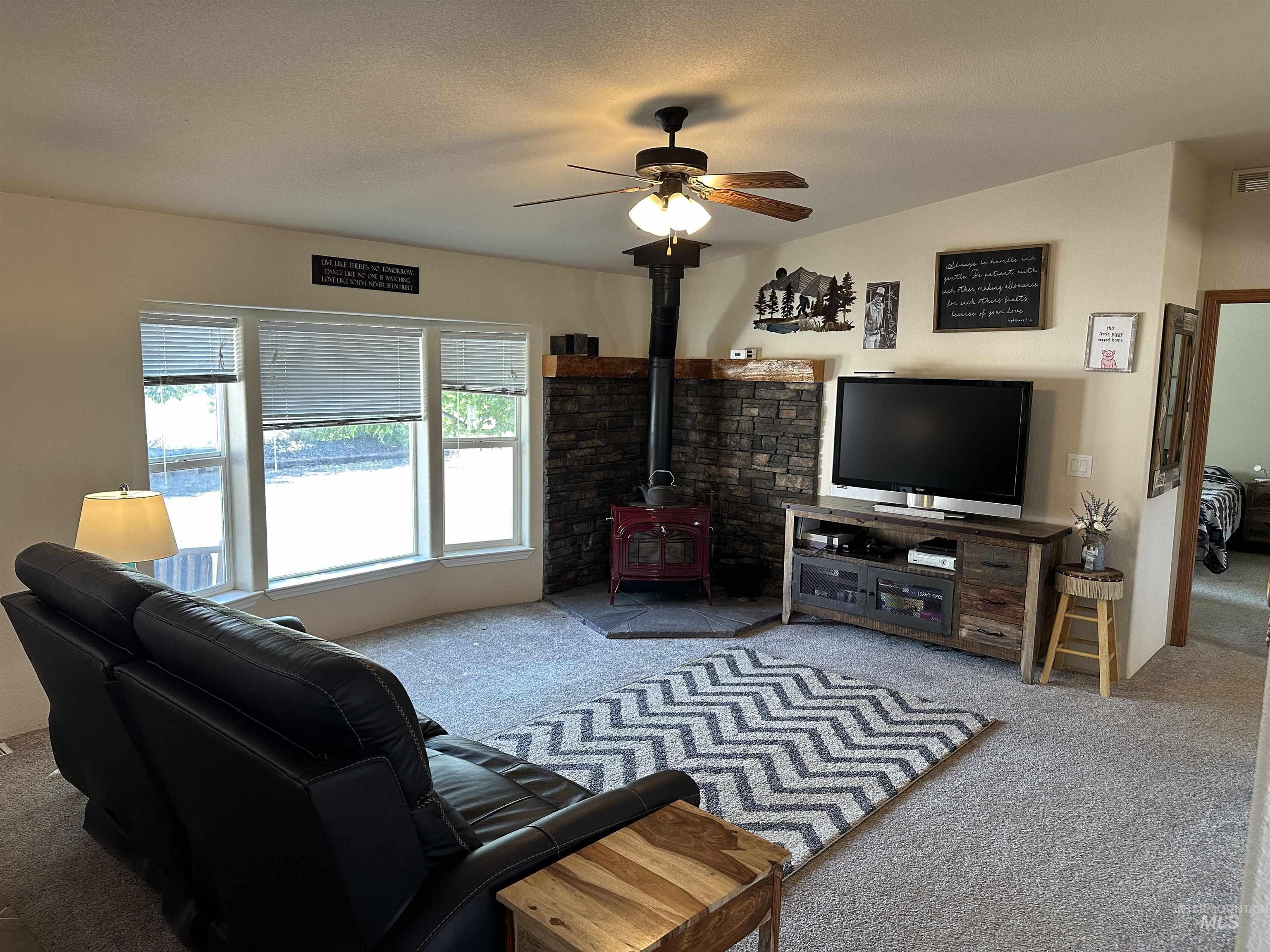 Carpeted living room with a wood stove and ceiling fan