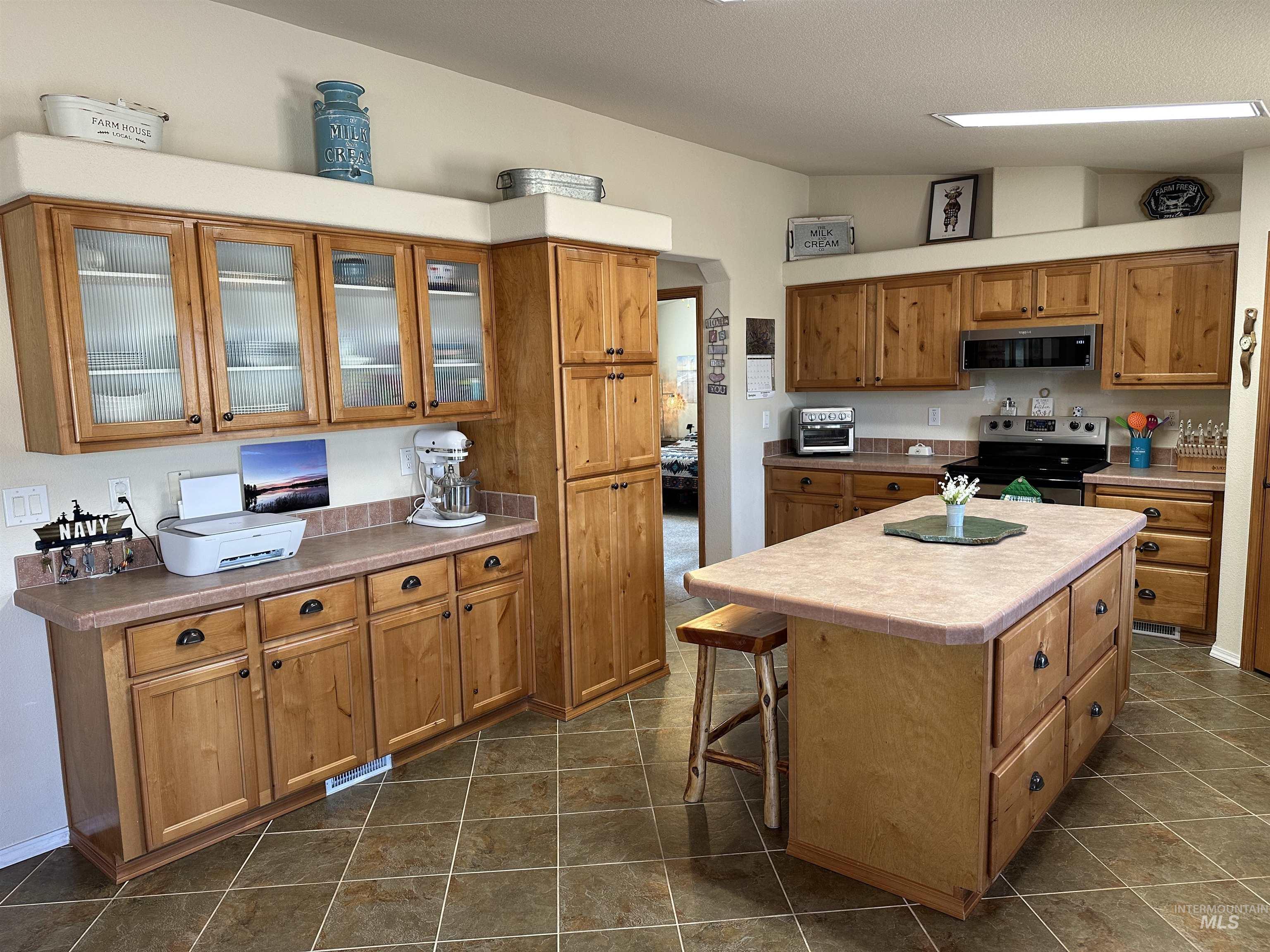 Kitchen featuring stainless steel appliances, a kitchen island, glass insert cabinets, brown cabinetry, and a breakfast bar area