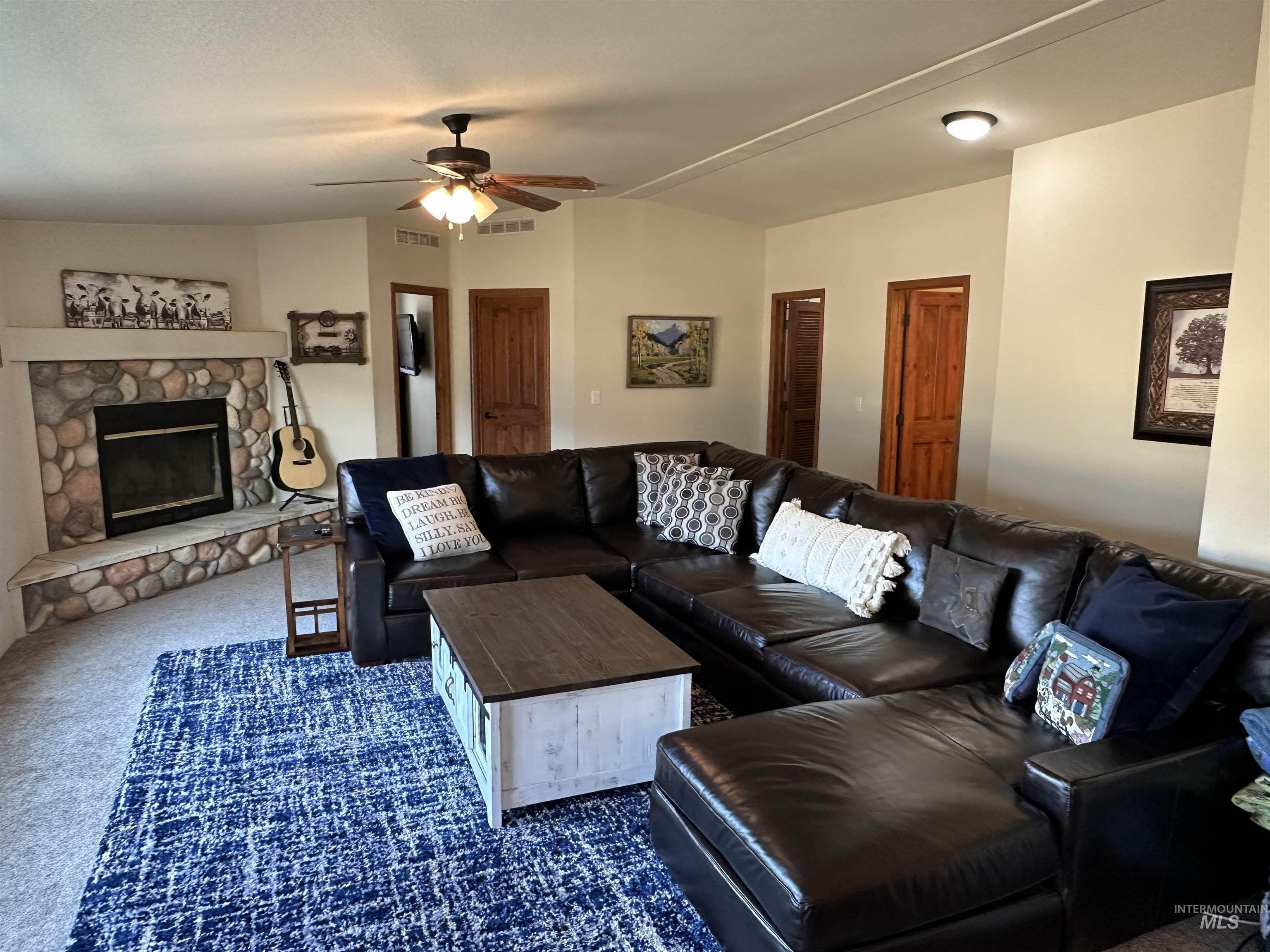 Living room featuring dark carpet, a fireplace, ceiling fan, and lofted ceiling