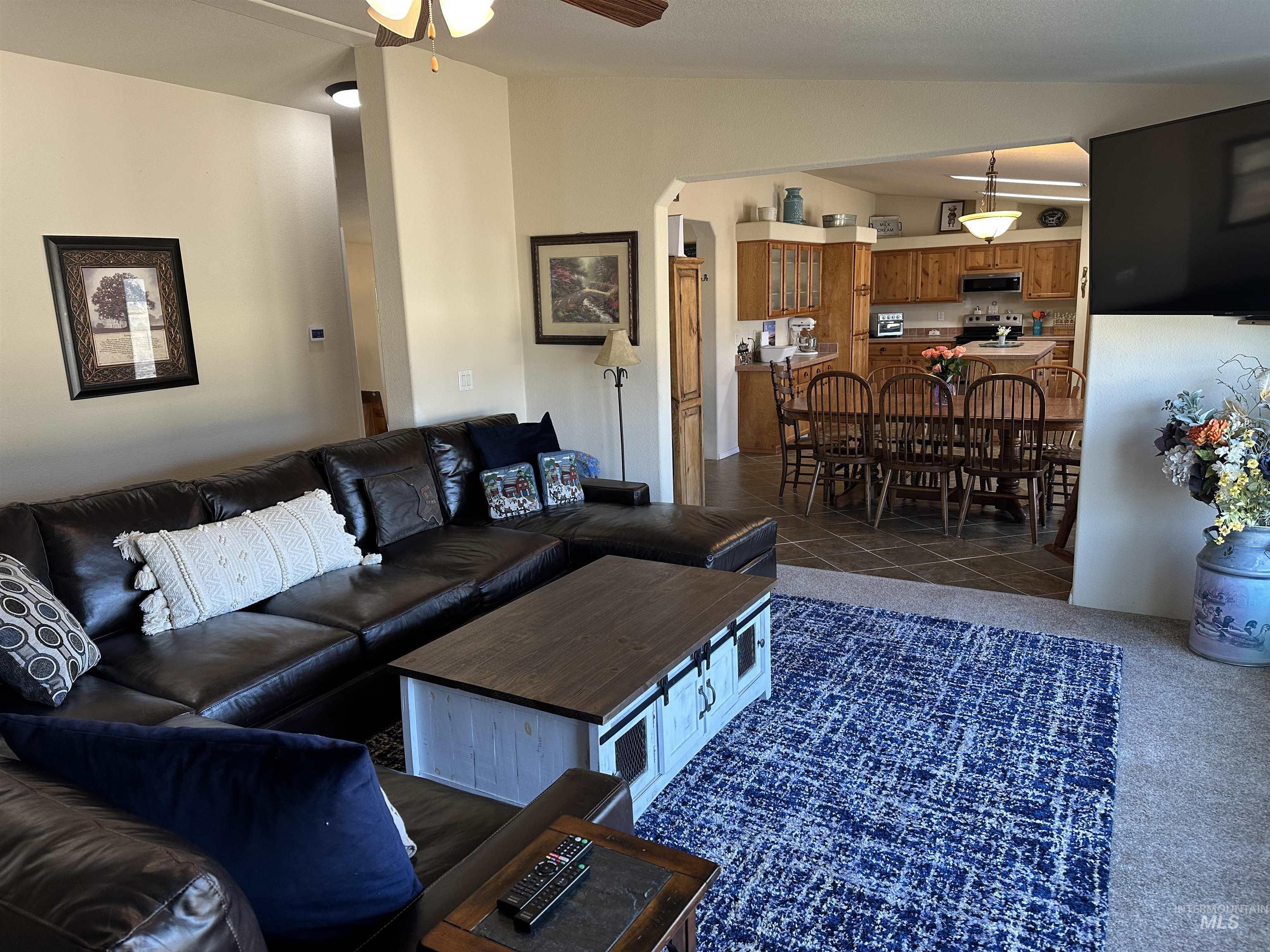 Living area featuring a ceiling fan, vaulted ceiling, dark tile patterned flooring, dark colored carpet, and arched walkways