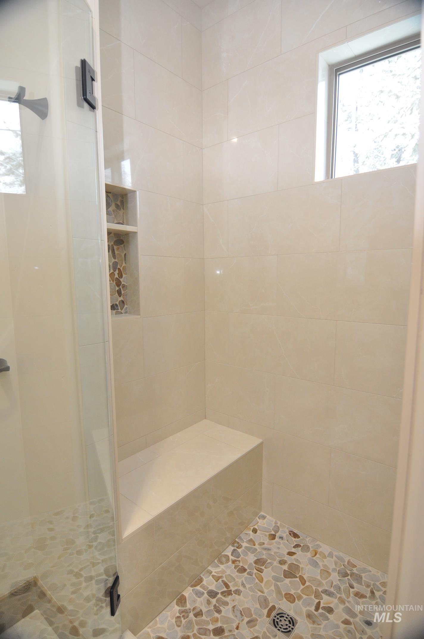 Walk in shower with pebble accent tile, tiled bench and window.
