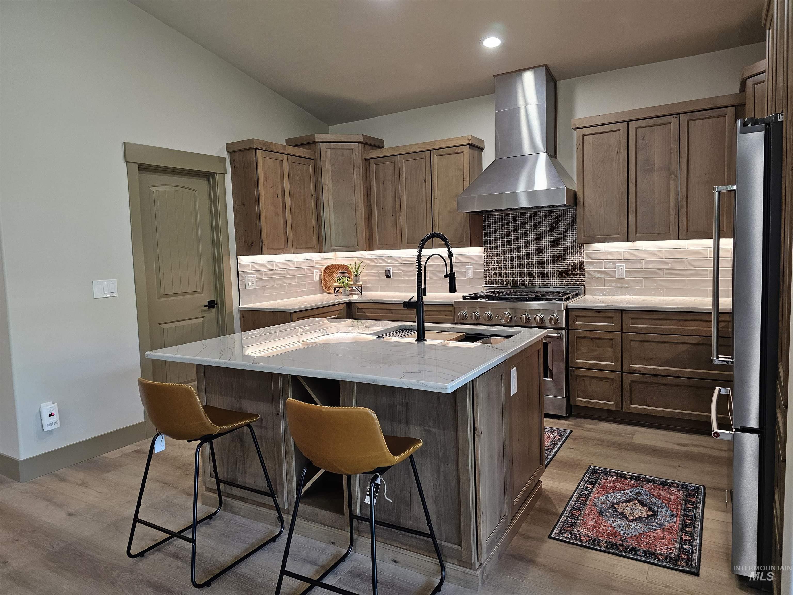 Kitchen with wall chimney exhaust hood, stainless steel appliances, gas range, tile backsplash and recessed lighting