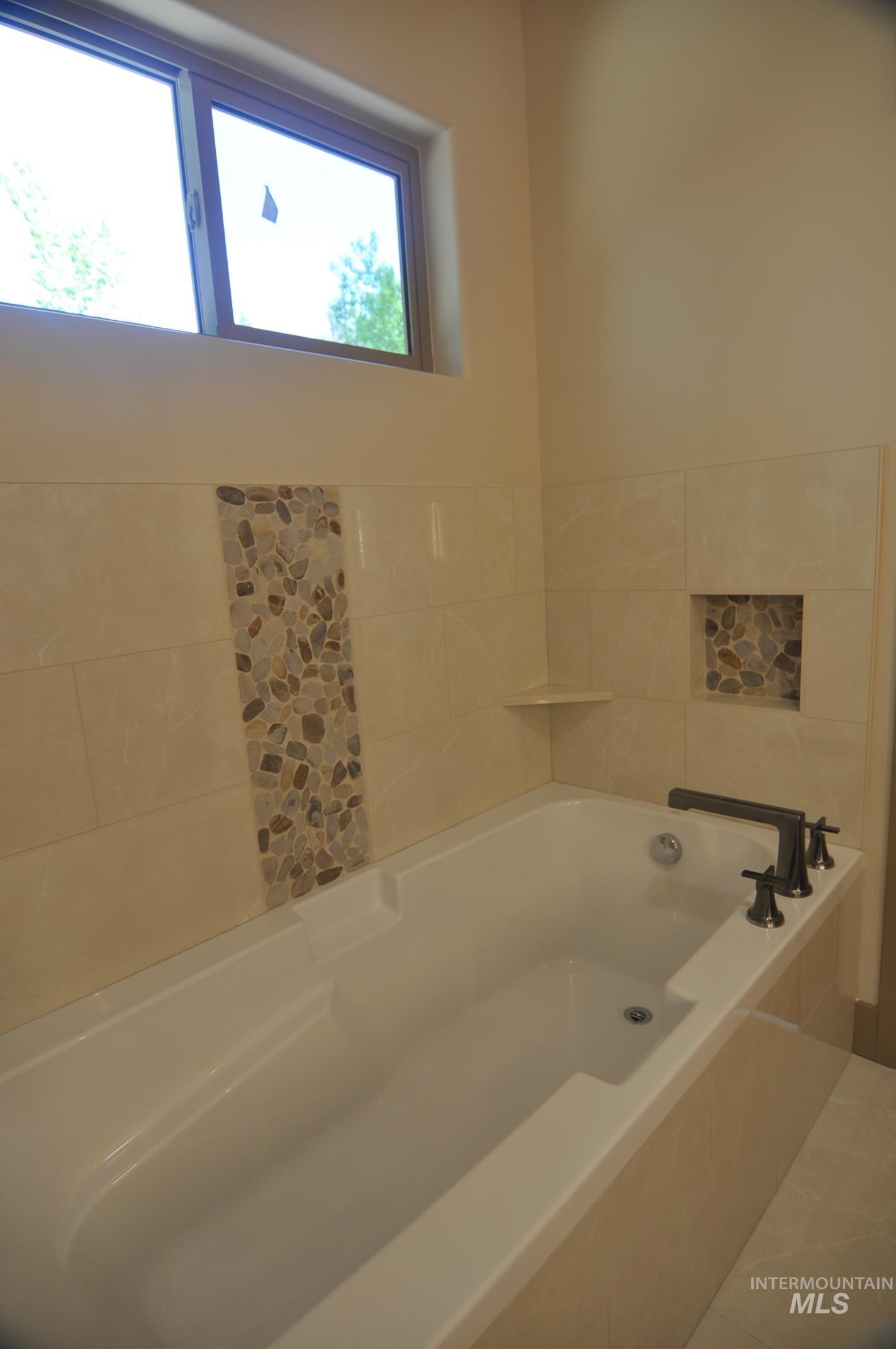 Large soaker tub with tile surround and pebble accent tile.