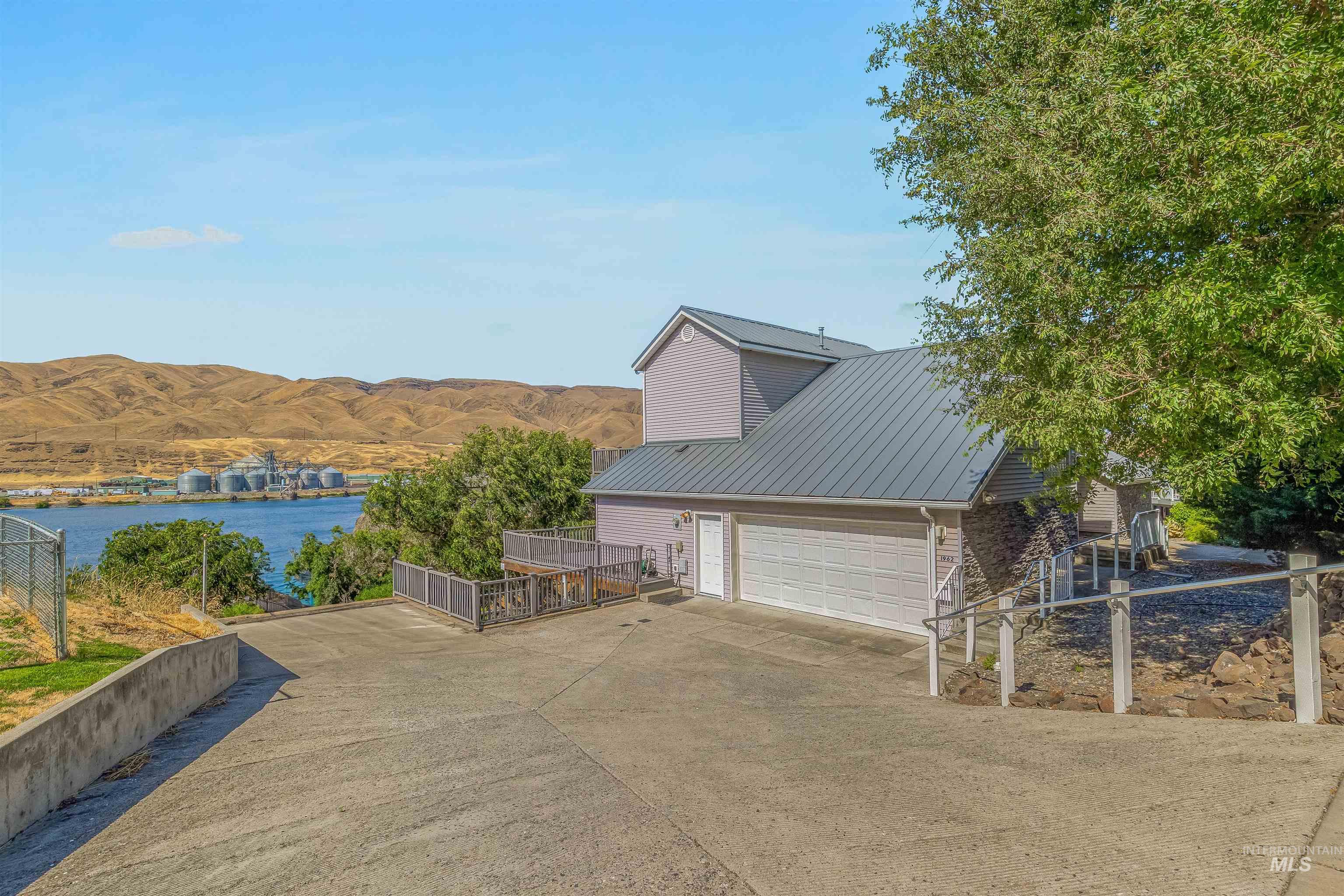 View of property exterior featuring a metal roof, a water and mountain view, driveway, a garage, and stone siding