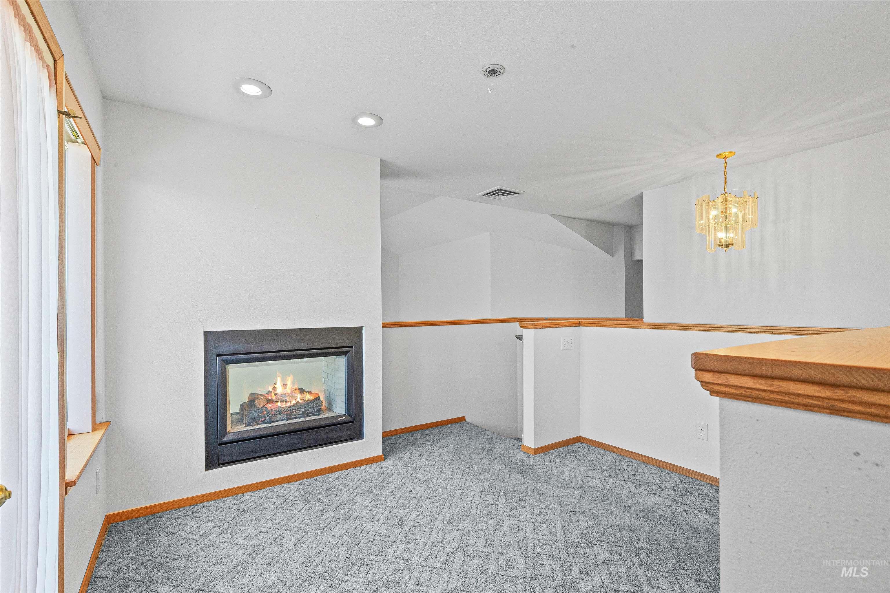 Unfurnished living room with a chandelier, a warm lit fireplace, recessed lighting, and carpet flooring