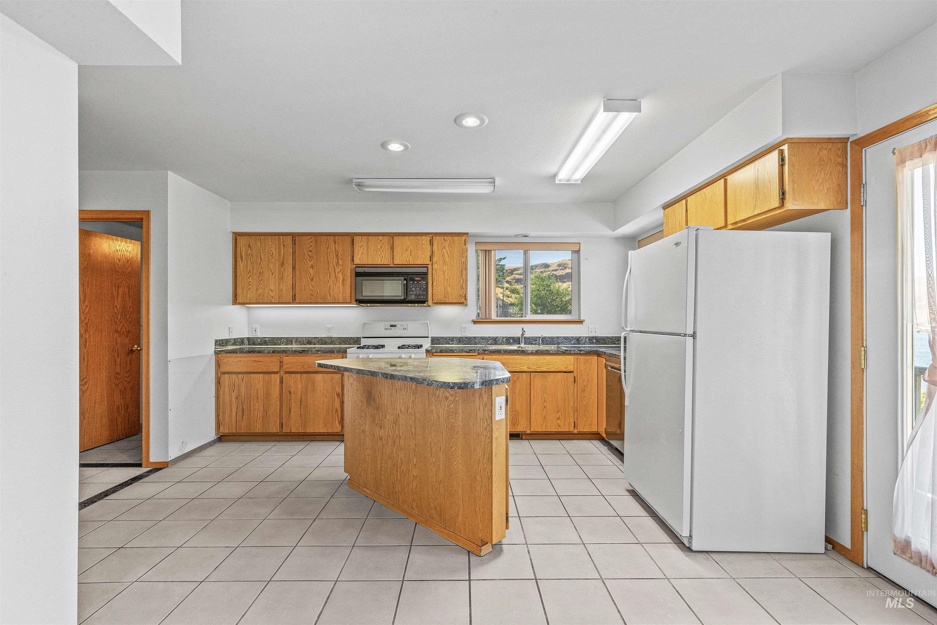 Kitchen with white appliances, a kitchen island, dark countertops, recessed lighting, and light tile patterned floors
