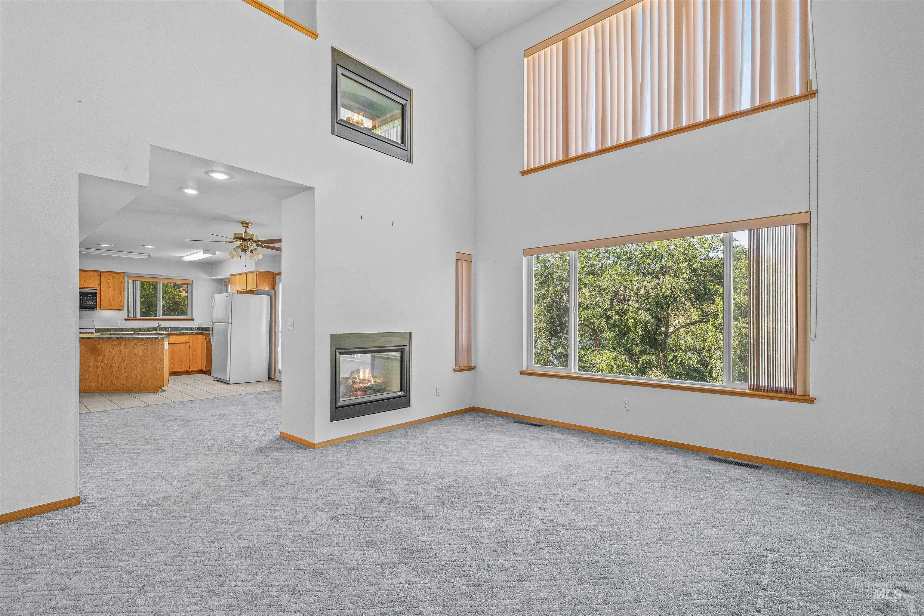 Unfurnished living room with plenty of natural light, light carpet, a towering ceiling, a ceiling fan, and a multi sided fireplace
