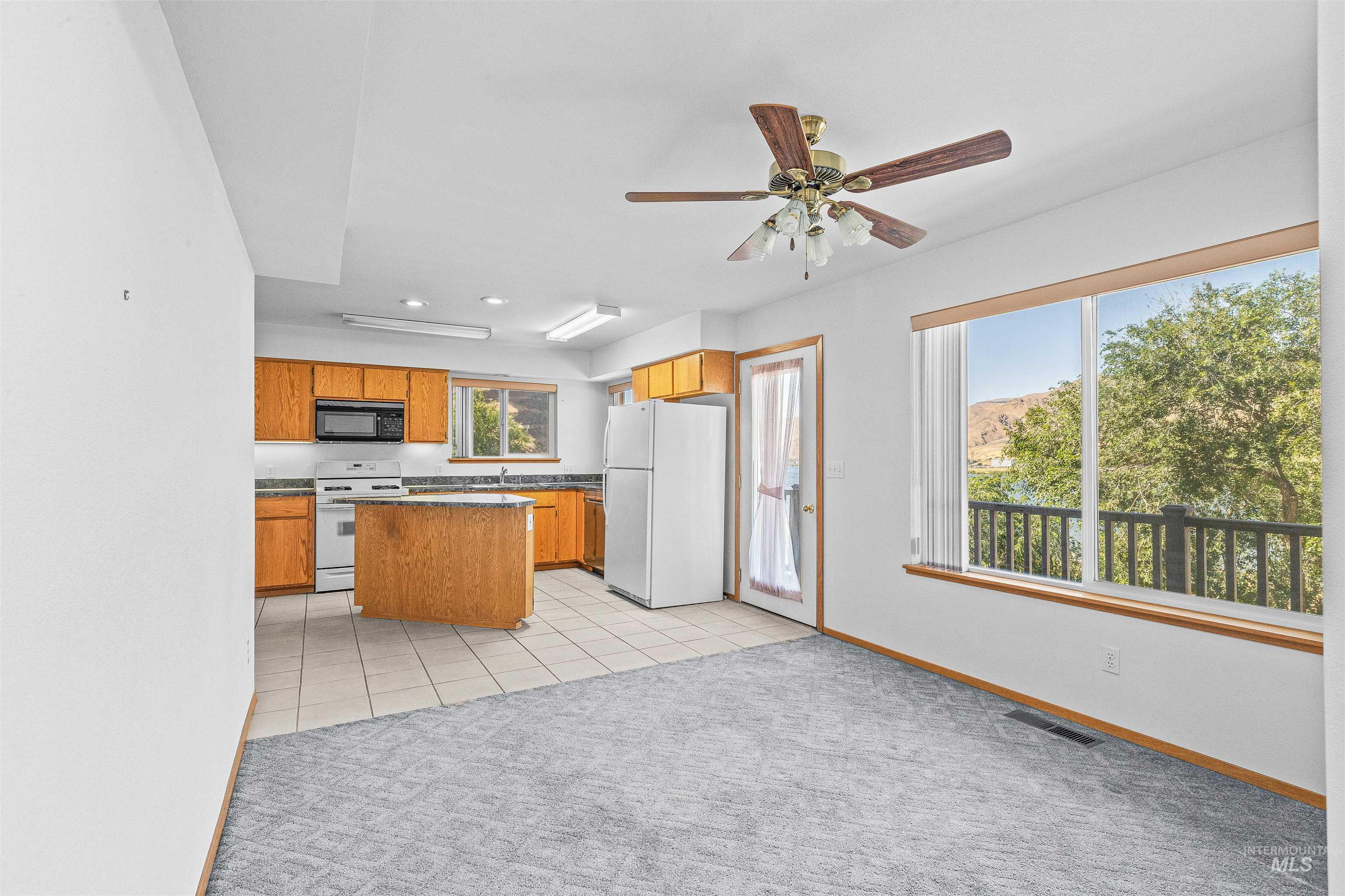 Kitchen featuring white appliances, light carpet, brown cabinetry, dark countertops, and ceiling fan