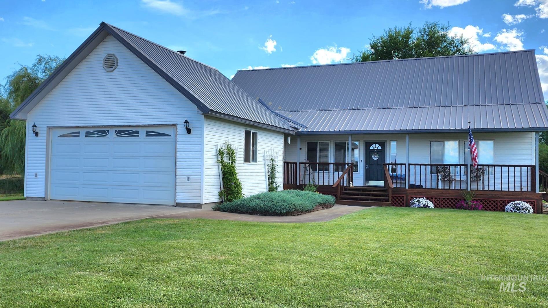 Two story home with a front lawn, covered porch, an attached garage, concrete driveway, and a metal roof