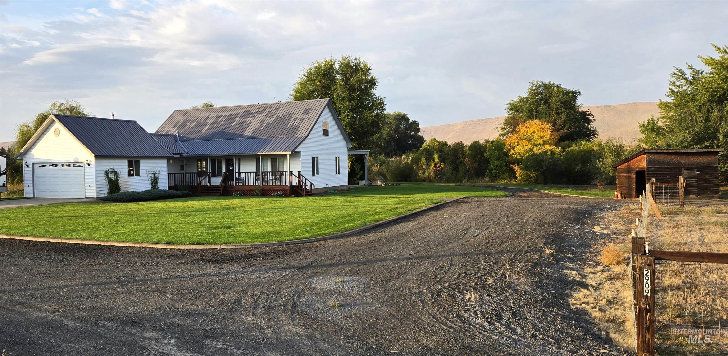 View of front of property featuring driveway, a front yard, a metal roof, a garage, and an outbuilding