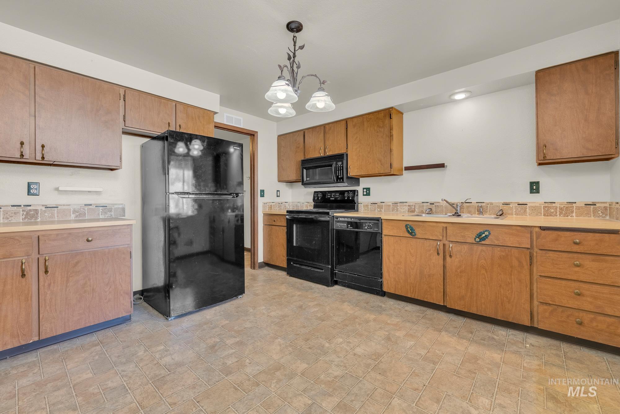 Kitchen featuring black appliances, light countertops, hanging light fixtures, and brown cabinets