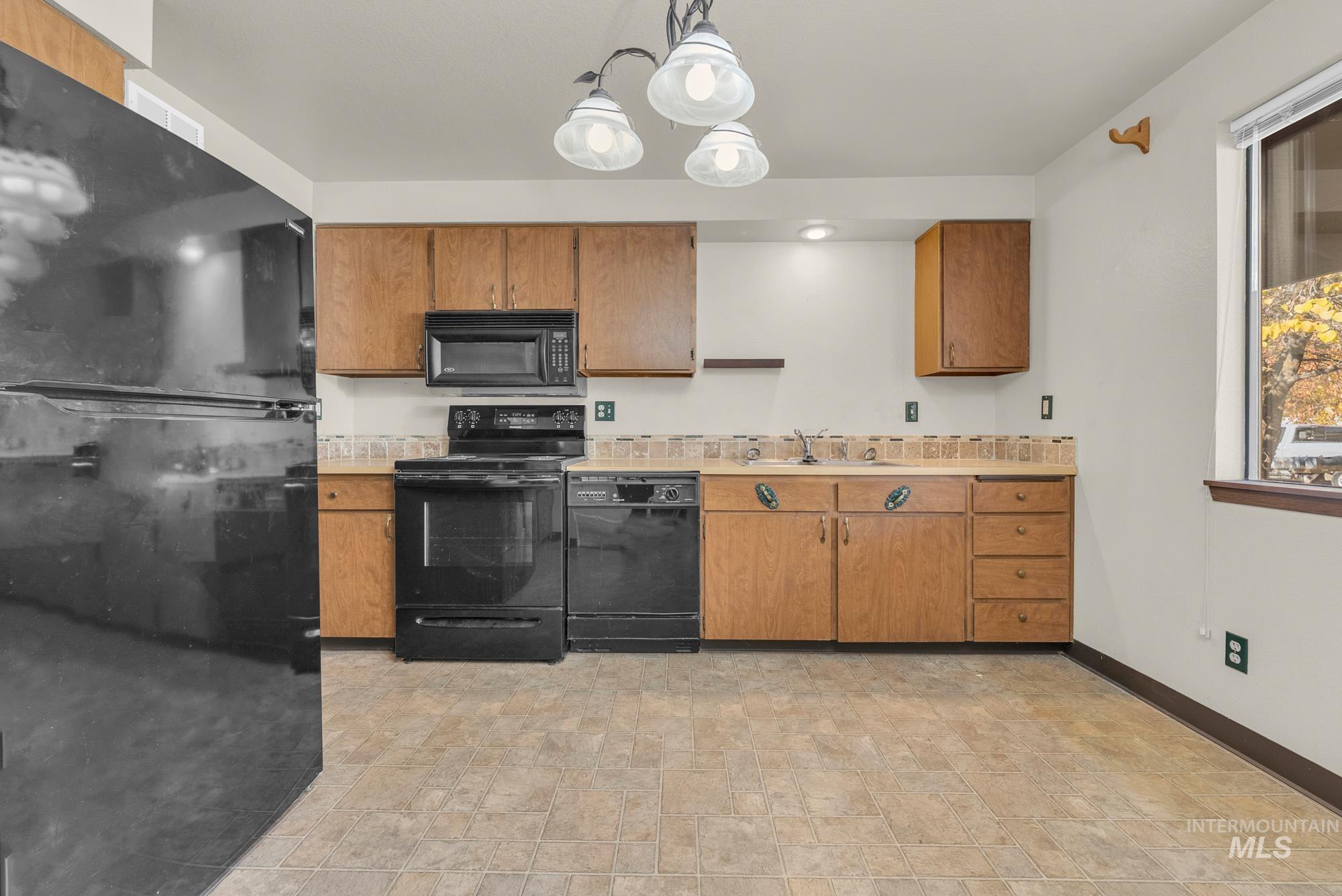 Kitchen featuring black appliances, brown cabinets, pendant lighting, and stone finish flooring