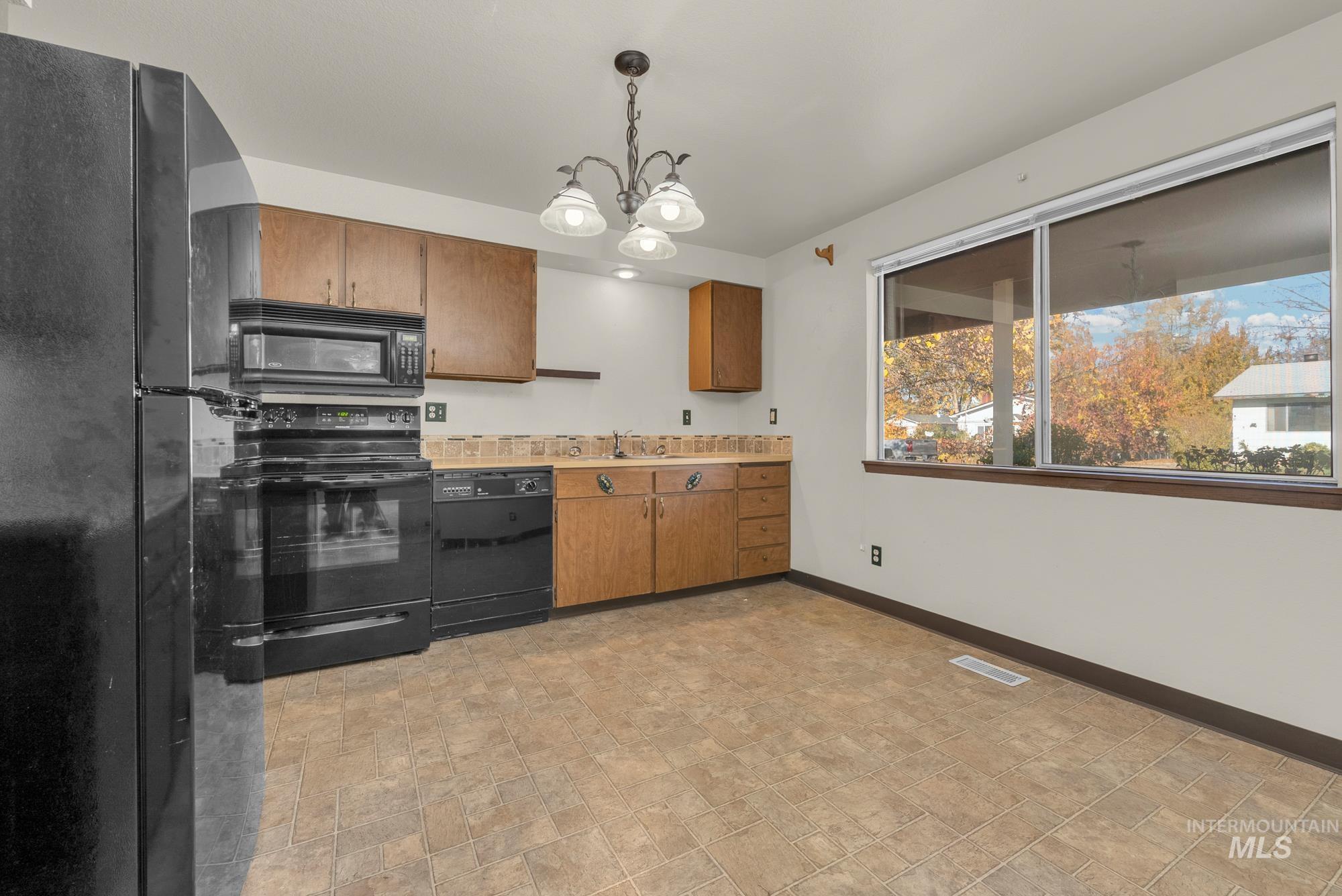 Kitchen with black appliances, decorative light fixtures, light countertops, and brown cabinetry