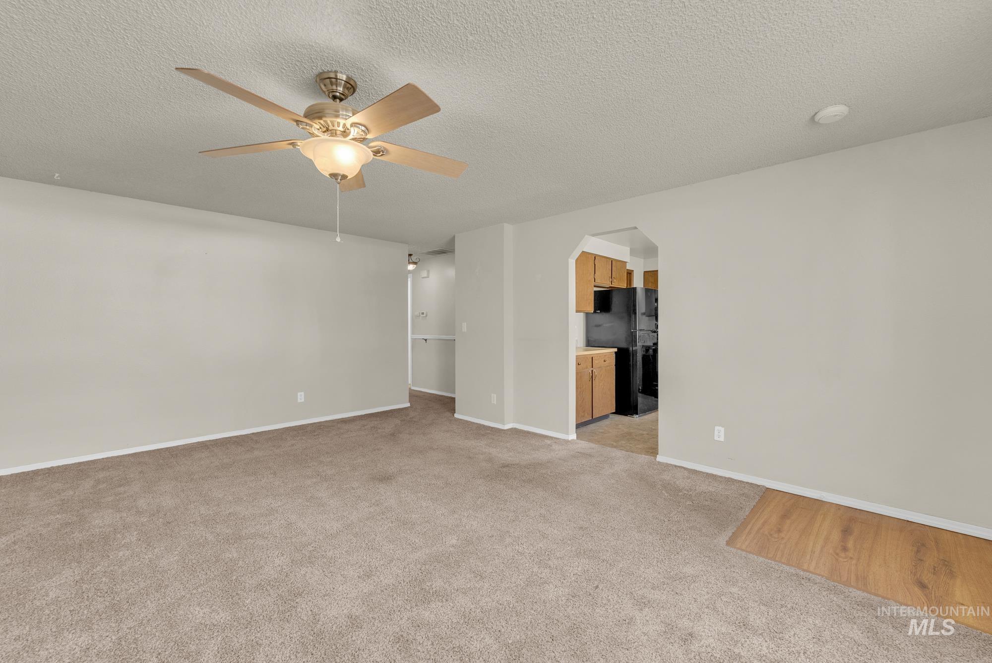 Unfurnished room with a textured ceiling, light colored carpet, ceiling fan, and arched walkways