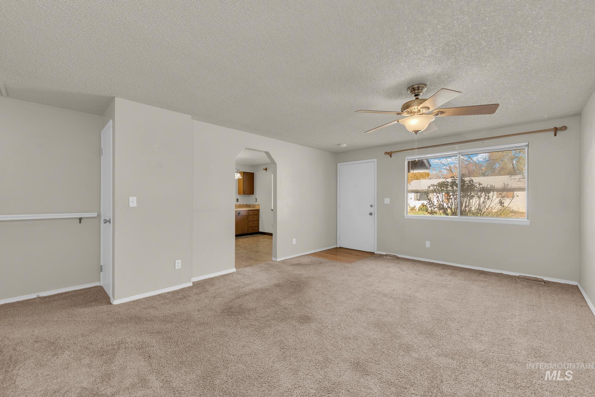 Empty room with light carpet, arched walkways, a textured ceiling, and a ceiling fan