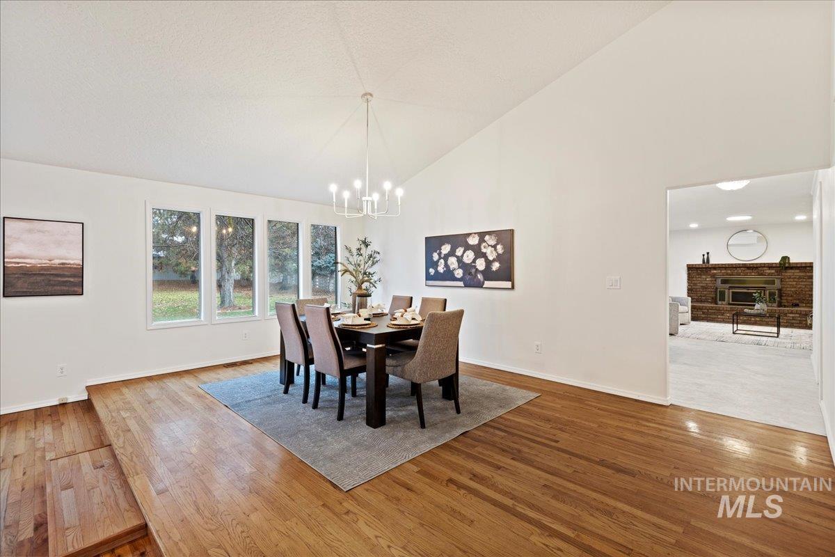 Dining area with high vaulted ceiling, a fireplace, hardwood / wood-style floors, and a chandelier