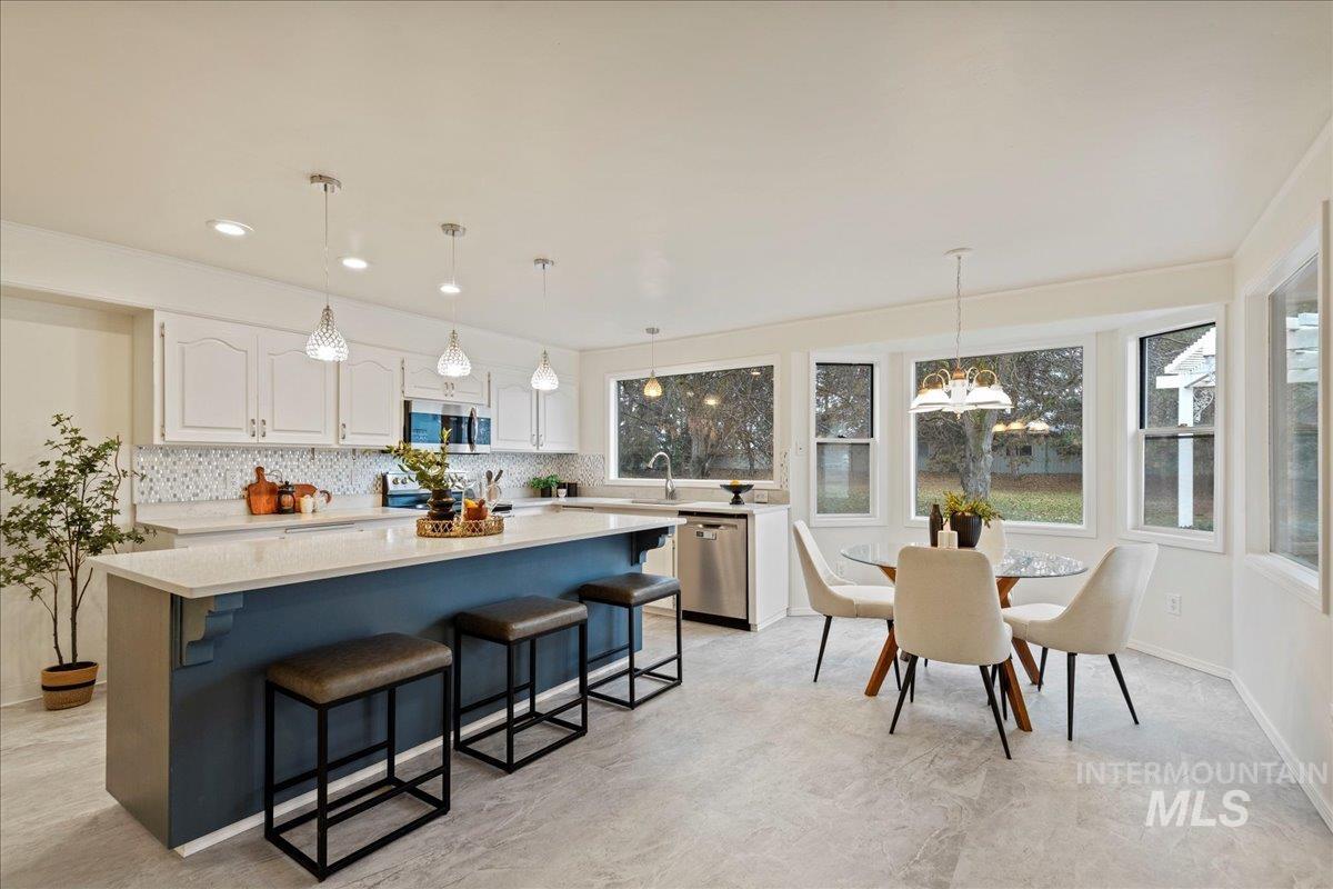 Kitchen featuring white cabinets, a kitchen island, decorative light fixtures, a breakfast bar area, and appliances with stainless steel finishes