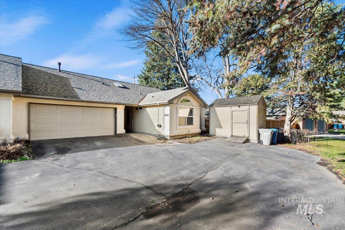 View of front of property with a storage unit, driveway, a shingled roof, and a garage