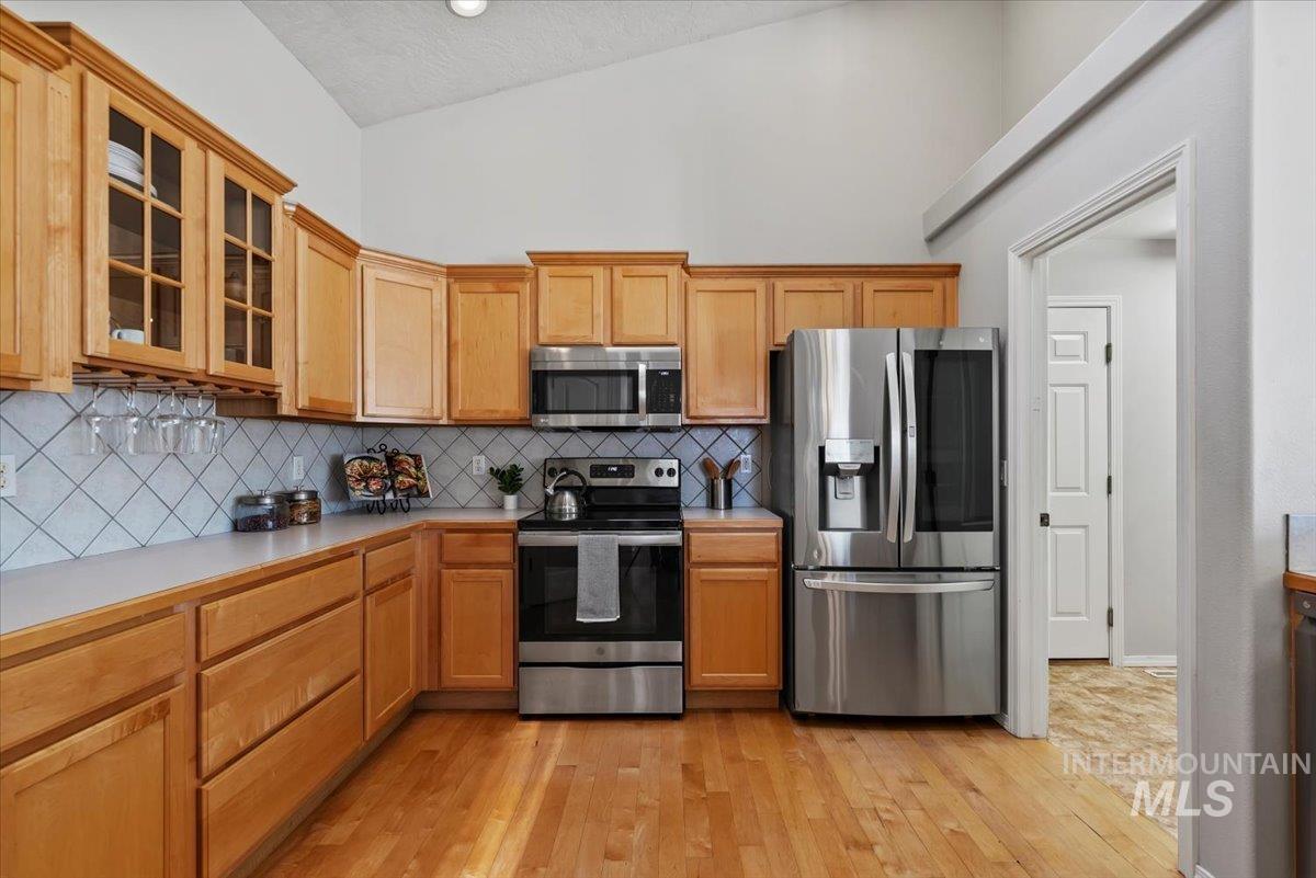 Kitchen featuring stainless steel appliances, glass insert cabinets, light countertops, decorative backsplash, and light wood-style floors