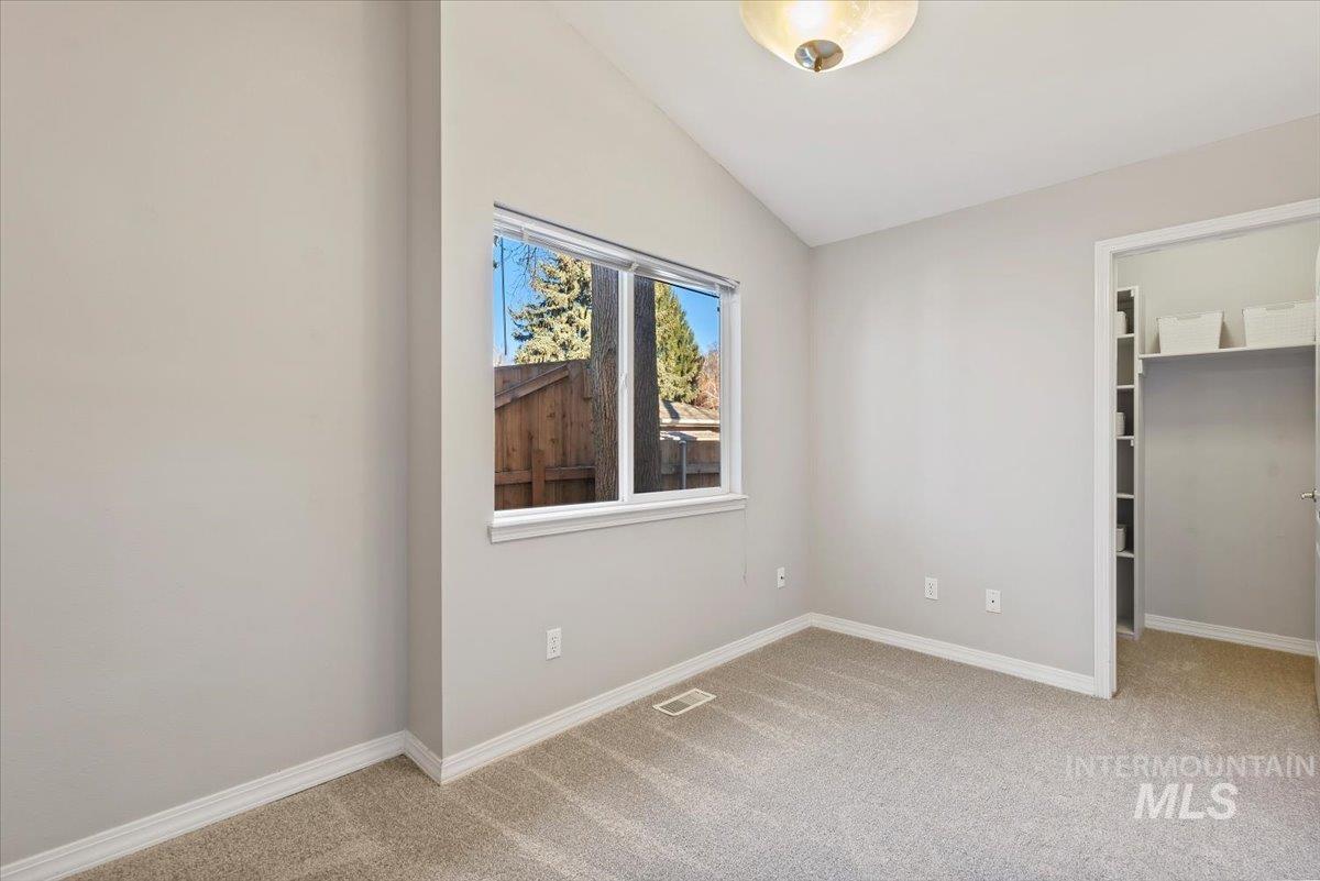 Unfurnished bedroom with a spacious closet, lofted ceiling, and light colored carpet