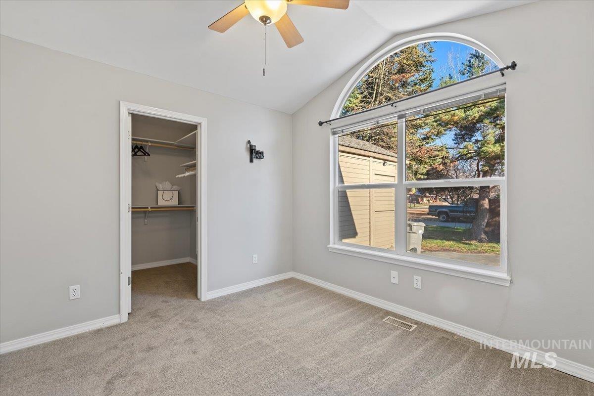 Unfurnished bedroom with lofted ceiling, a spacious closet, light carpet, and a ceiling fan