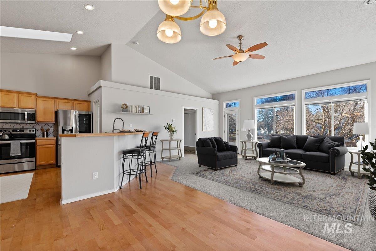 Living room with high vaulted ceiling, a skylight, light wood finished floors, a textured ceiling, and a ceiling fan