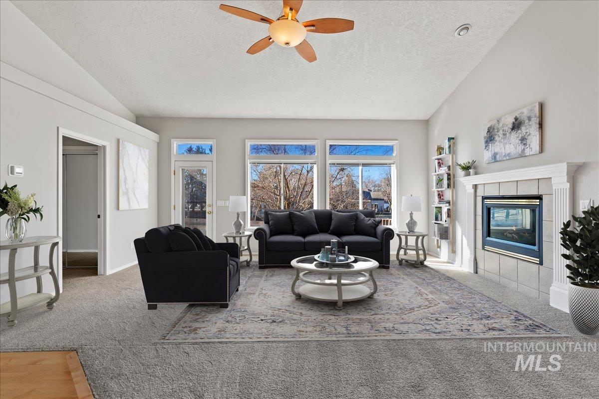 Carpeted living room with vaulted ceiling, a textured ceiling, a fireplace, and a ceiling fan