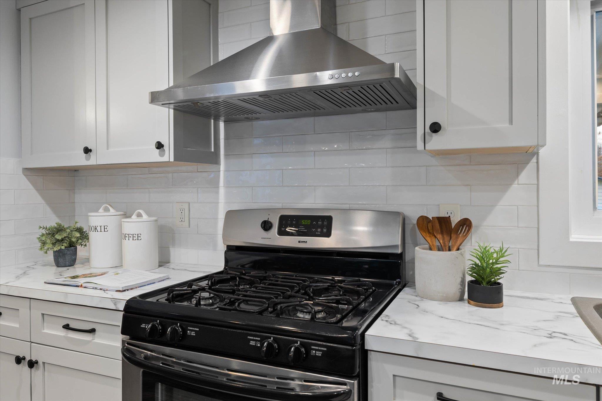 Kitchen featuring stainless steel range with gas cooktop, decorative backsplash, and white cabinets