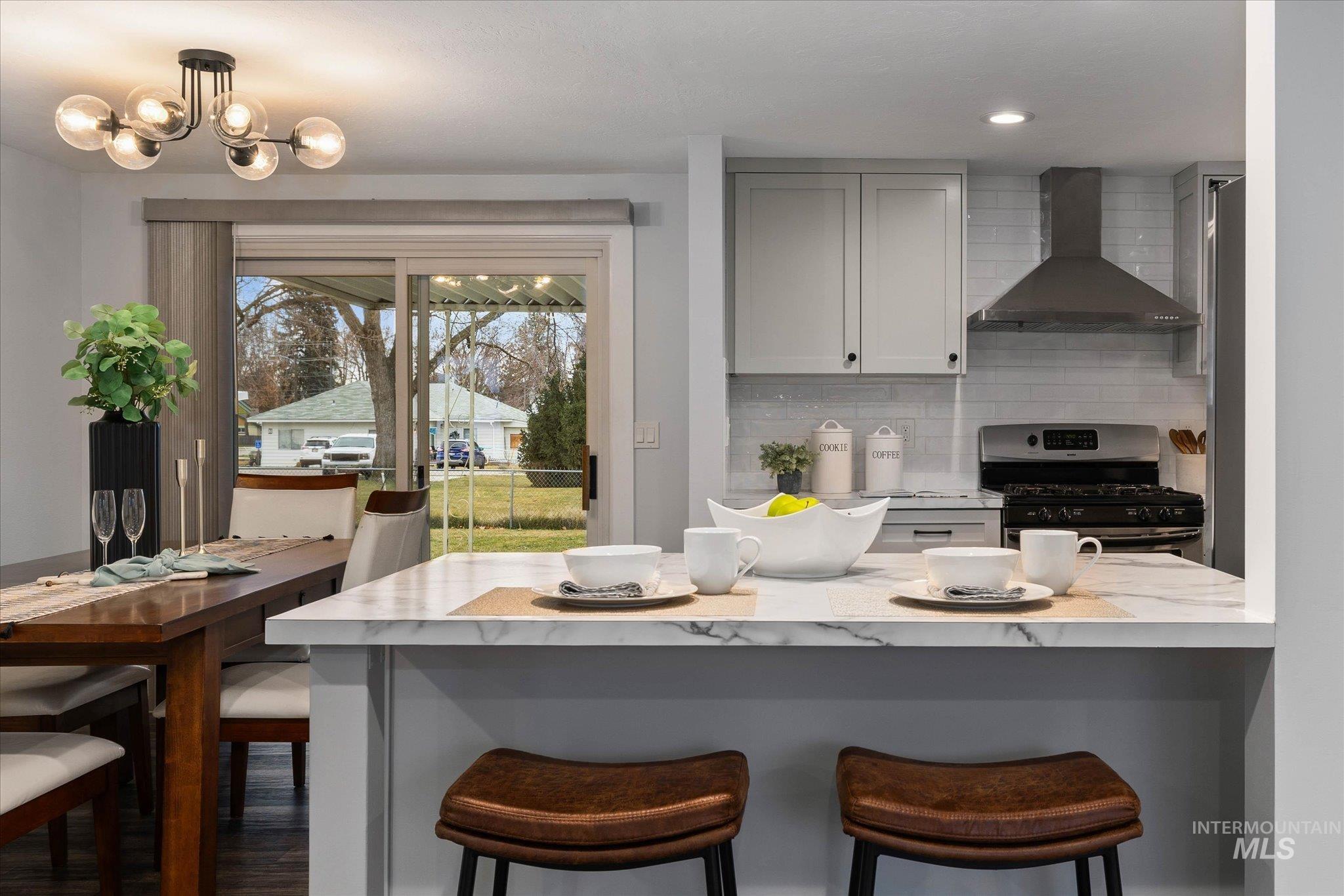 Kitchen featuring gas range, a kitchen bar, light stone countertops, gray cabinetry, and backsplash