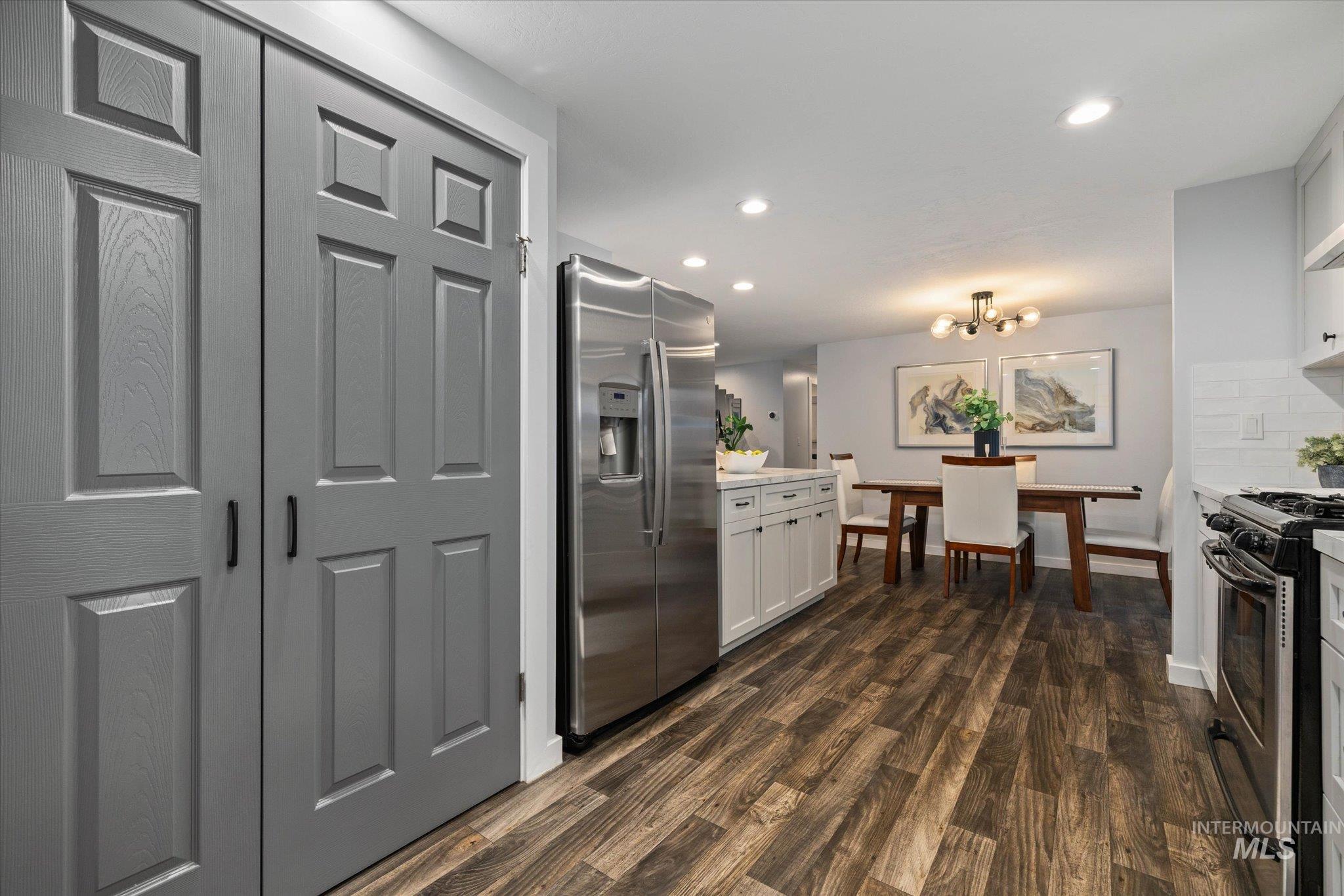 Kitchen with stainless steel appliances, dark wood-style floors, white cabinets, decorative backsplash, and a chandelier