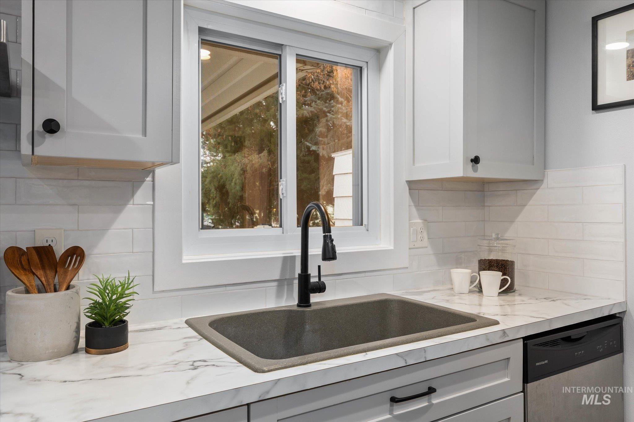 Kitchen featuring light countertops, stainless steel dishwasher, backsplash, and white cabinets