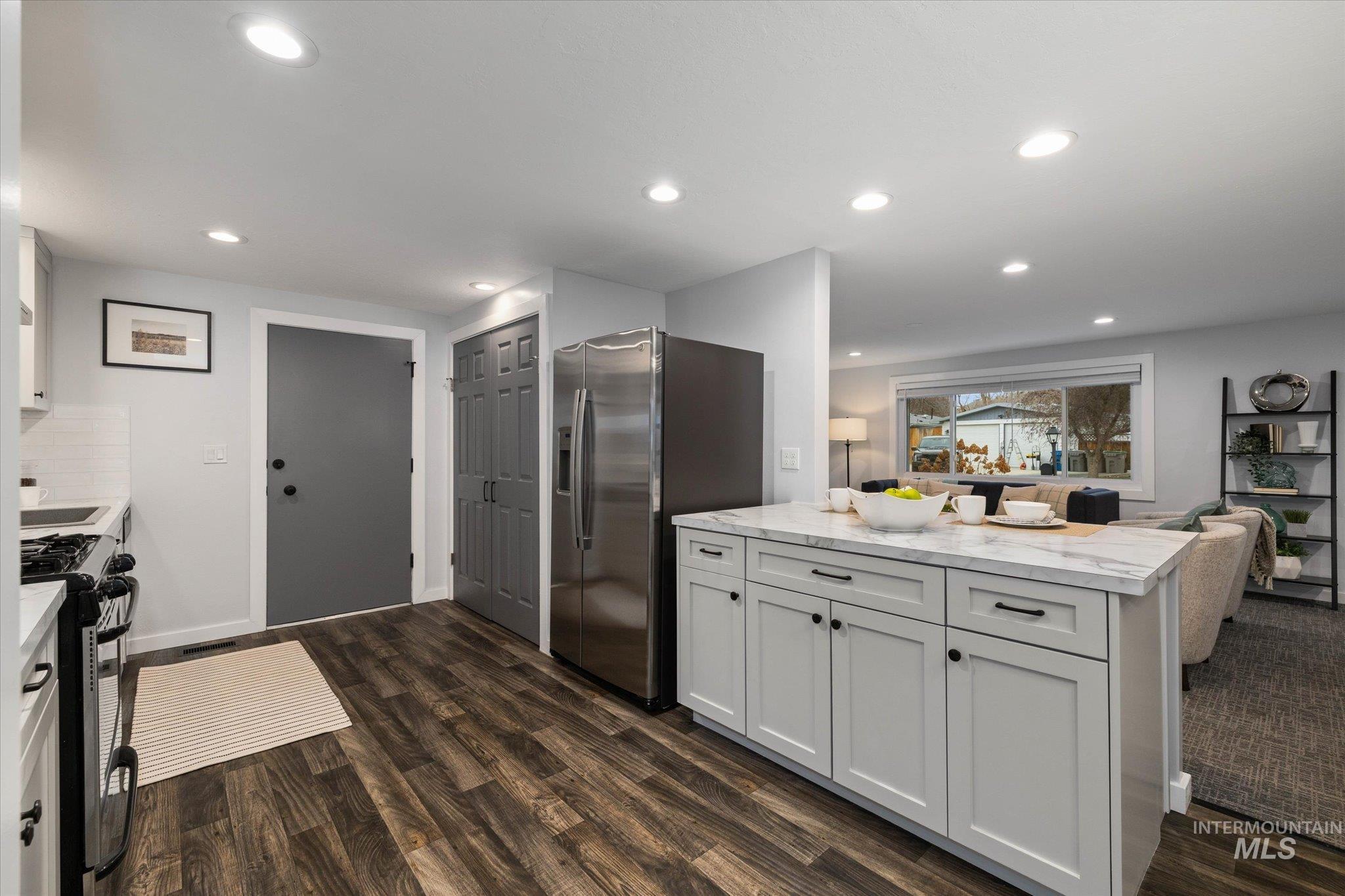 Kitchen featuring white cabinets, open floor plan, range with gas stovetop, stainless steel fridge with ice dispenser, and light stone countertops