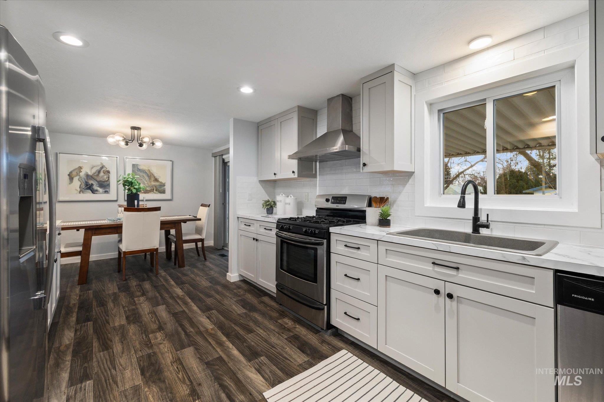 Kitchen with stainless steel appliances, dark wood-type flooring, decorative backsplash, suspended lighting, and light stone counters