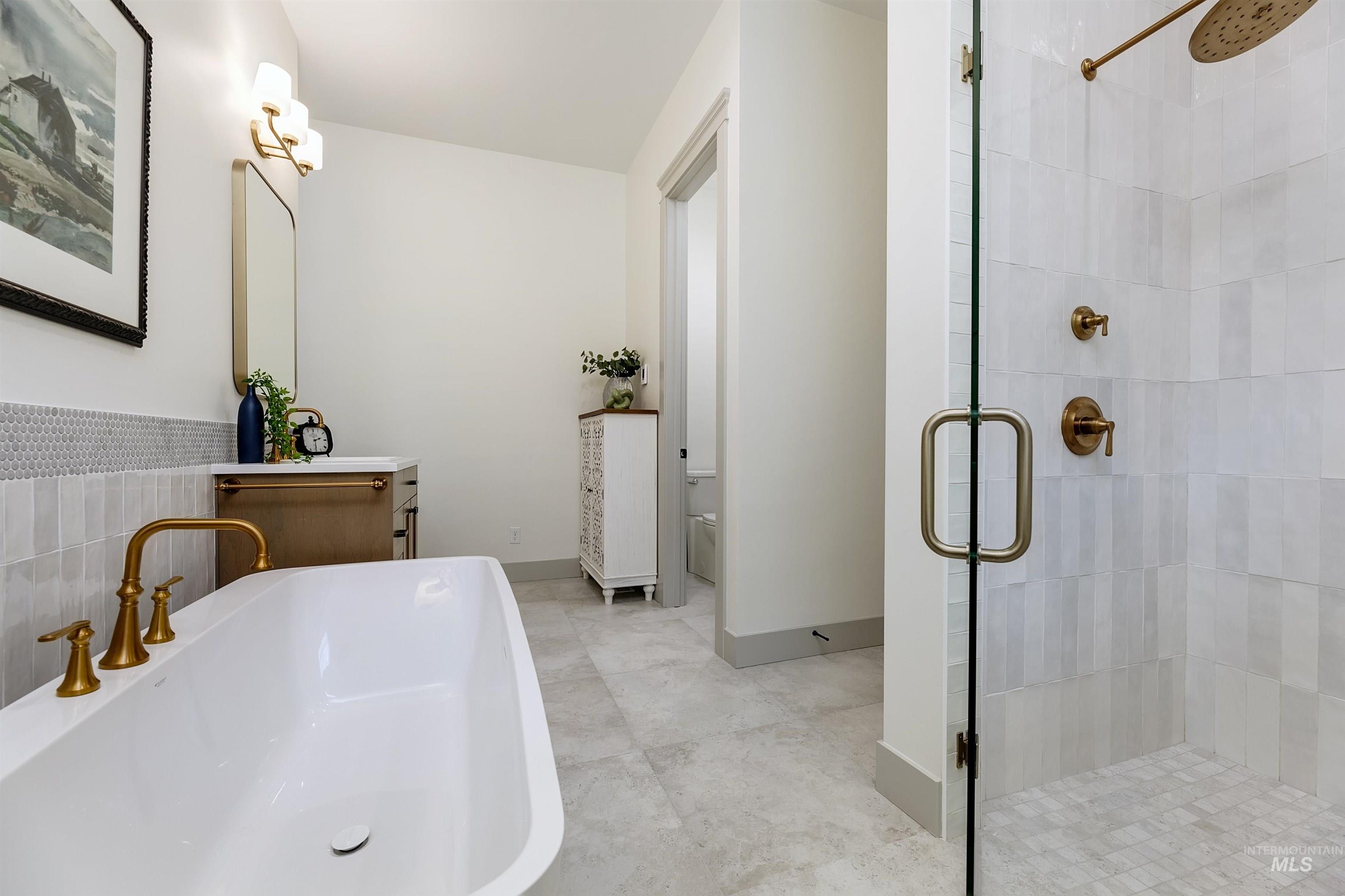 Freestanding bathtub with brass fixtures, glass-enclosed shower featuring a rainfall showerhead, and a vanity with a rectangular mirror and sconce lighting