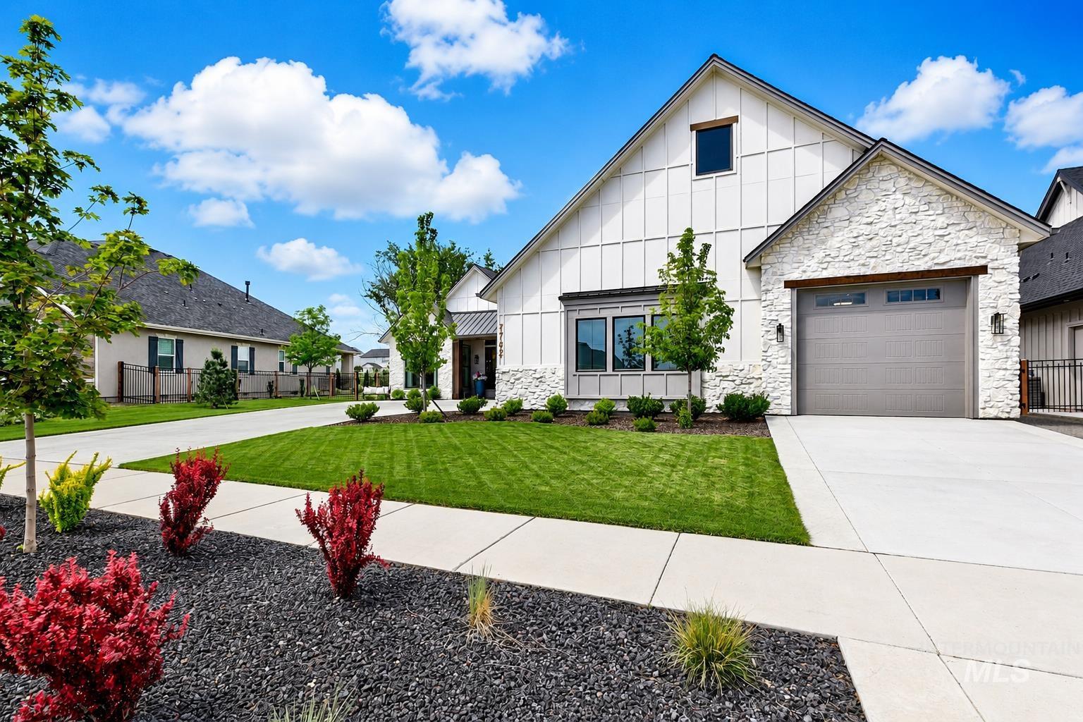 Contemporary farmhouse exterior featuring white board-and-batten siding, stone facade accents, an attached garage with a modern door, a covered entry, and a manicured front lawn with landscaping