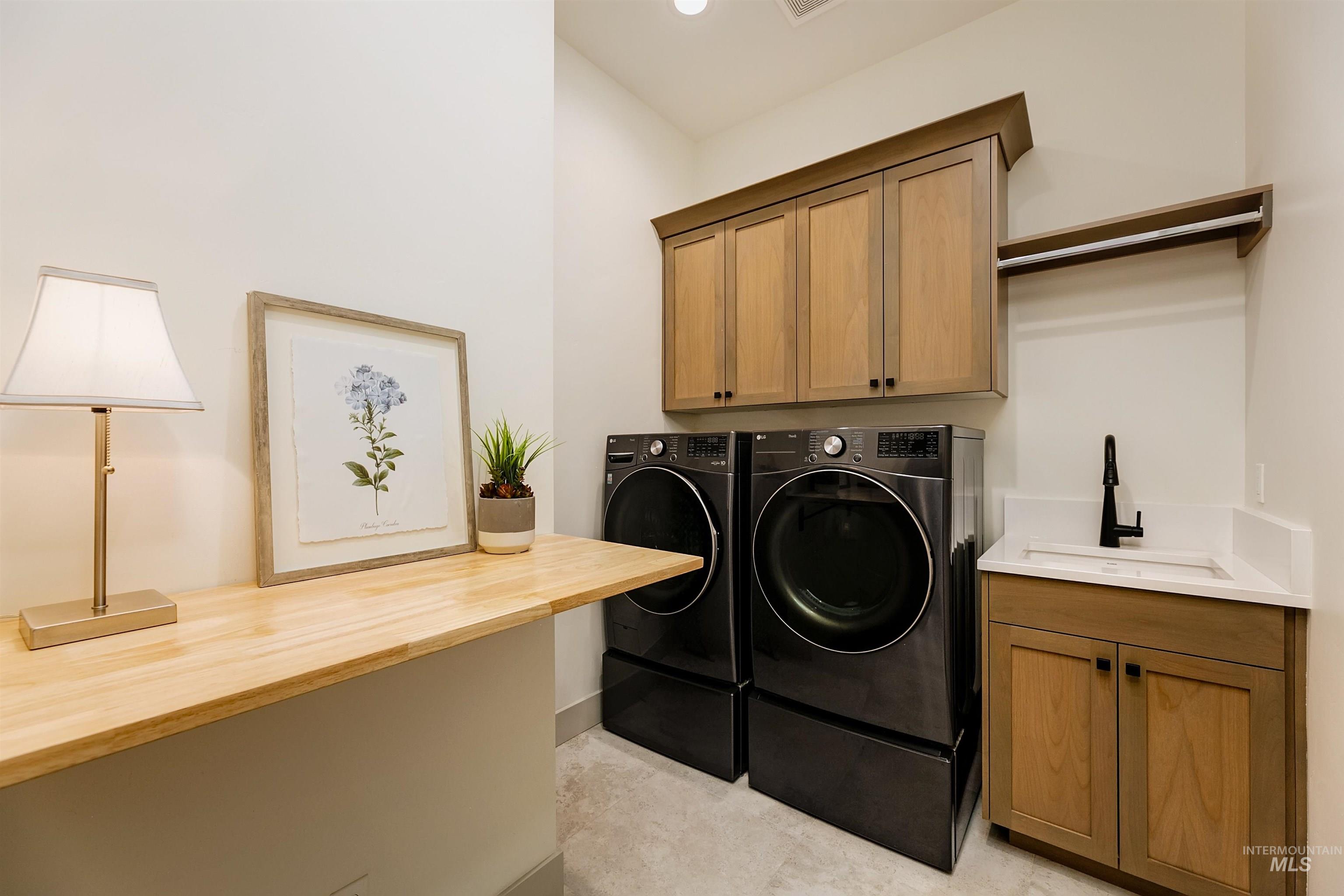 Dedicated laundry space featuring a built-in wood-finish countertop, coordinating upper and lower cabinetry, a utility sink with a matte black faucet, and a wall-mounted hanging rod