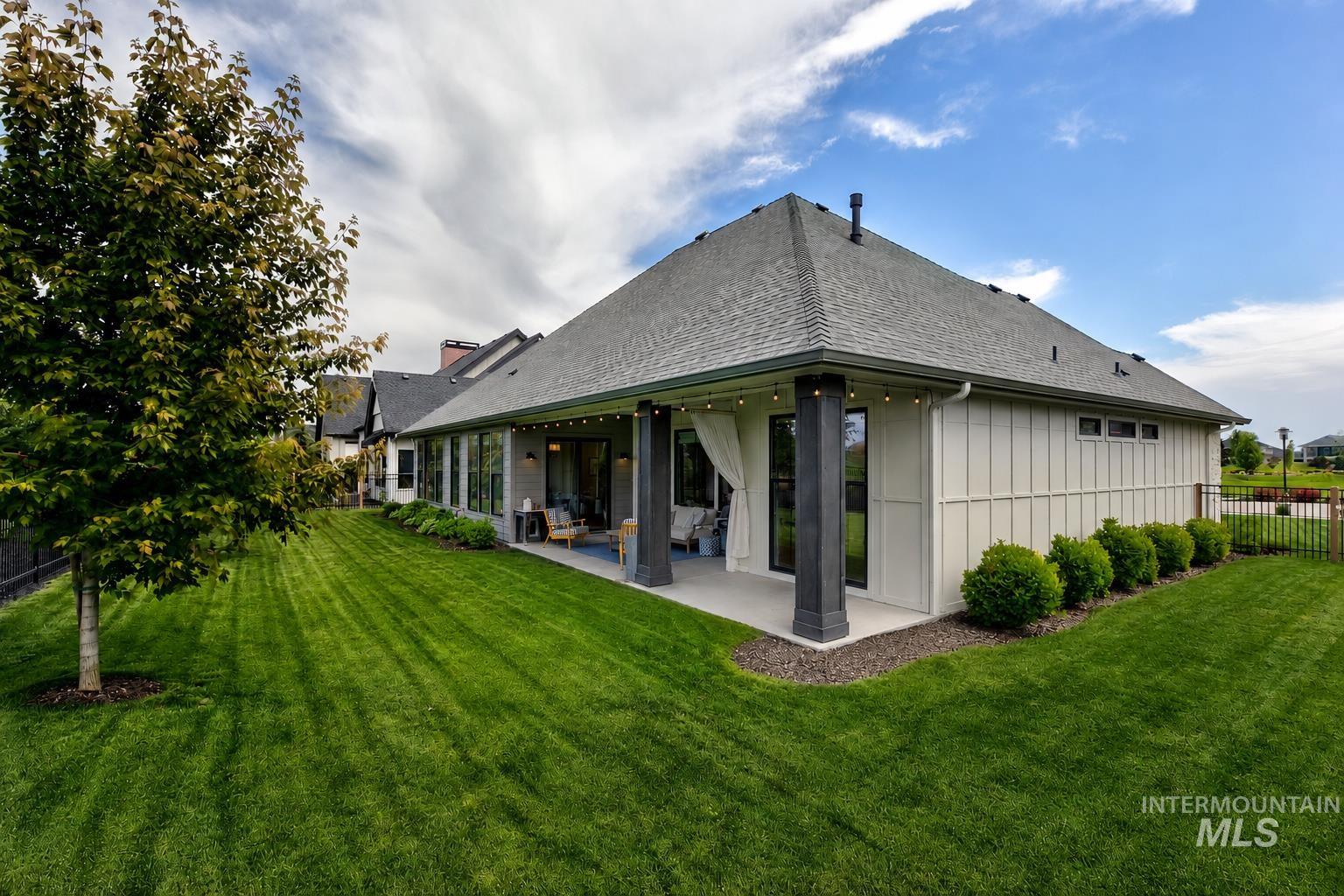 Expansive lawn with a covered patio featuring dark support columns, string lighting, and sheer white outdoor drapes
