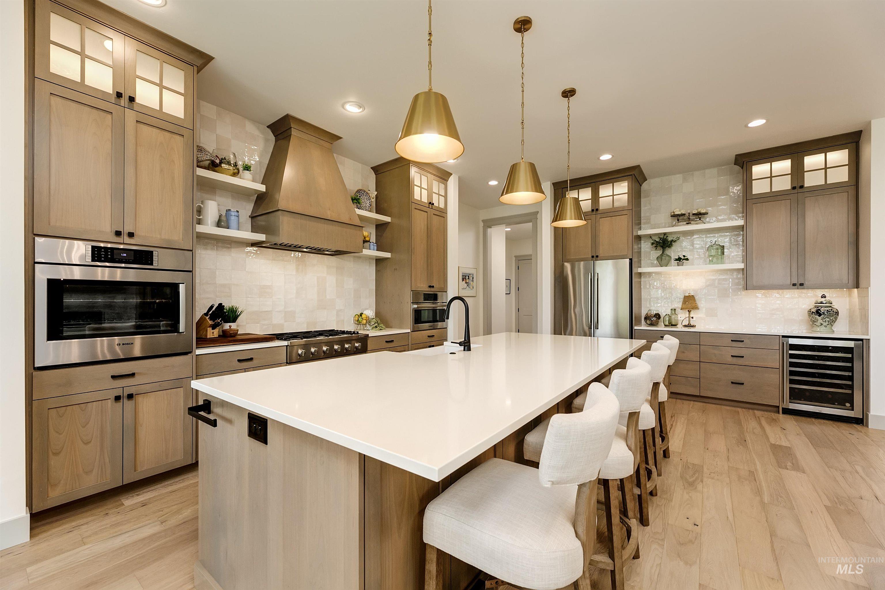 Spacious kitchen featuring a large central island with seating, stainless steel appliances, light wood-finish cabinetry, a built-in wine refrigerator, and light wood-finish flooring