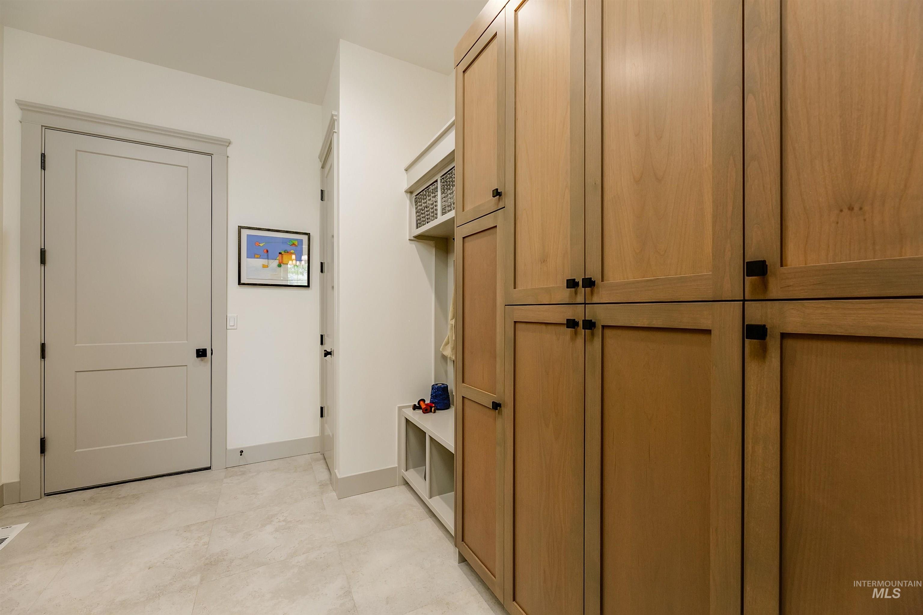 Built-in natural wood cabinetry with black hardware, light-toned tile flooring, light gray trim work, and a recessed cubby with integrated shelving