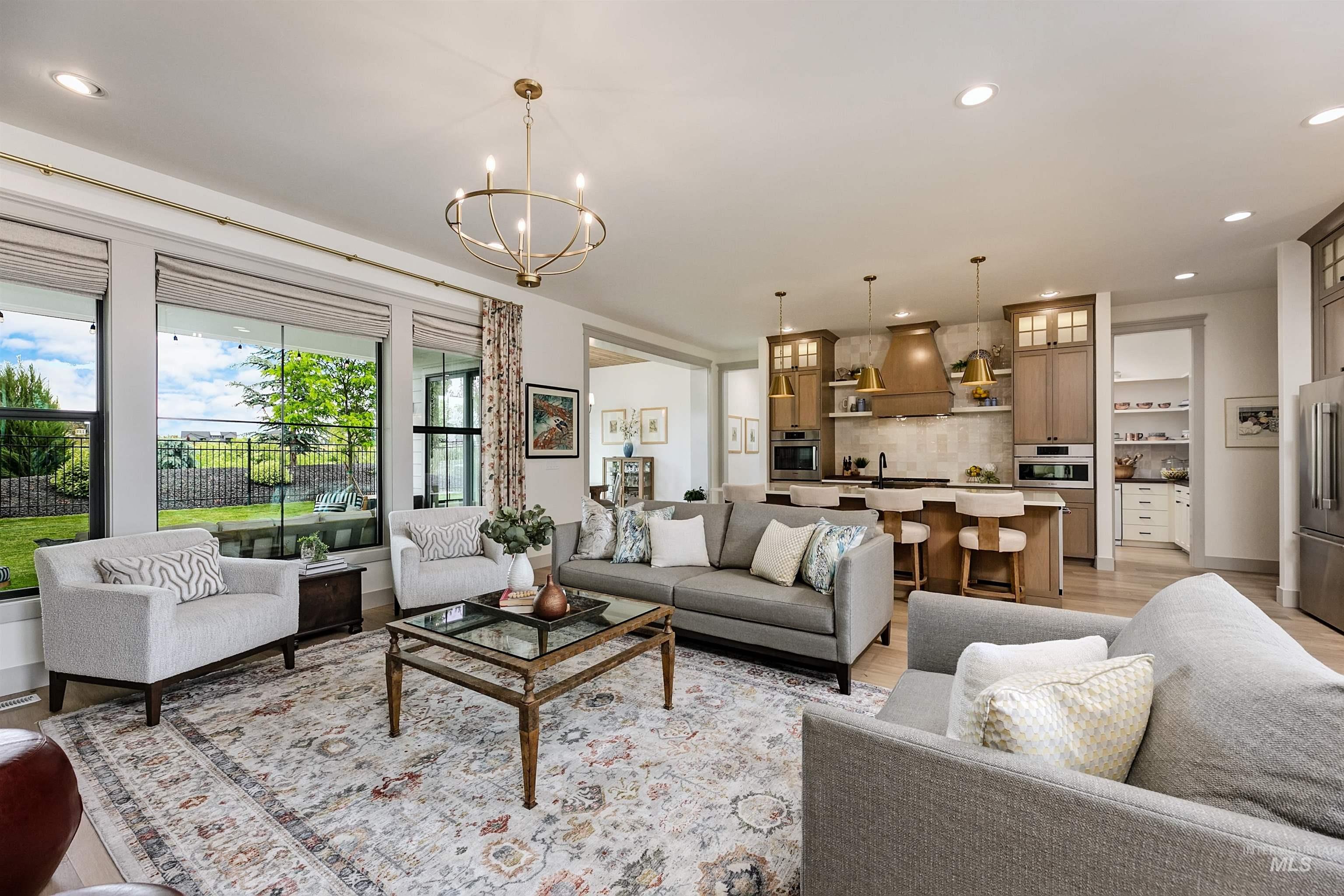 Open-concept living space featuring wood-finish flooring, a contemporary chandelier, and a kitchen with an island, built-in appliances, and warm-toned cabinetry