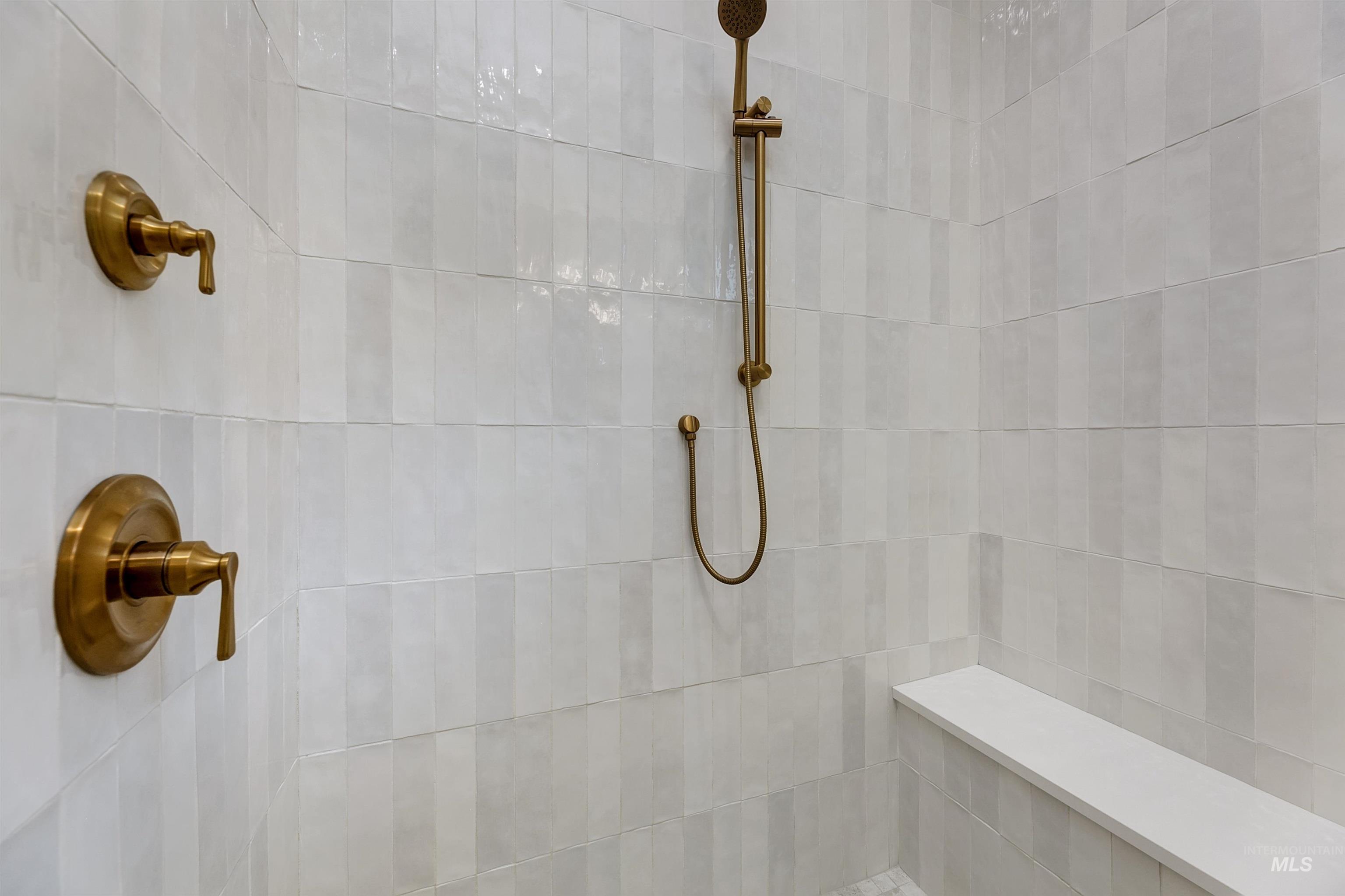 Shower stall featuring vertical white tile work, a built-in bench, and bronze fixtures