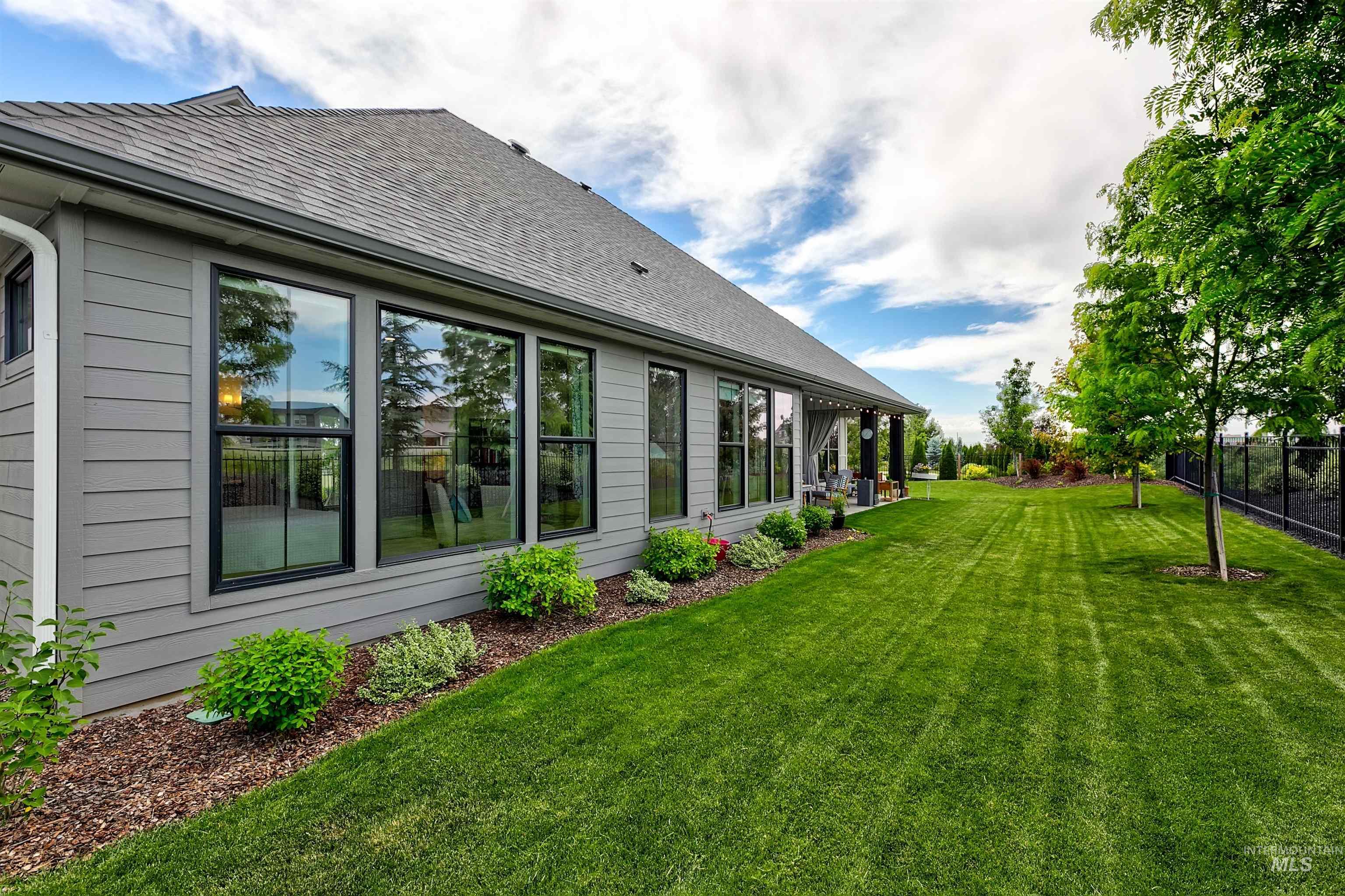 Spacious backyard featuring an expansive lawn, mature trees, and a covered patio area with dark pillars