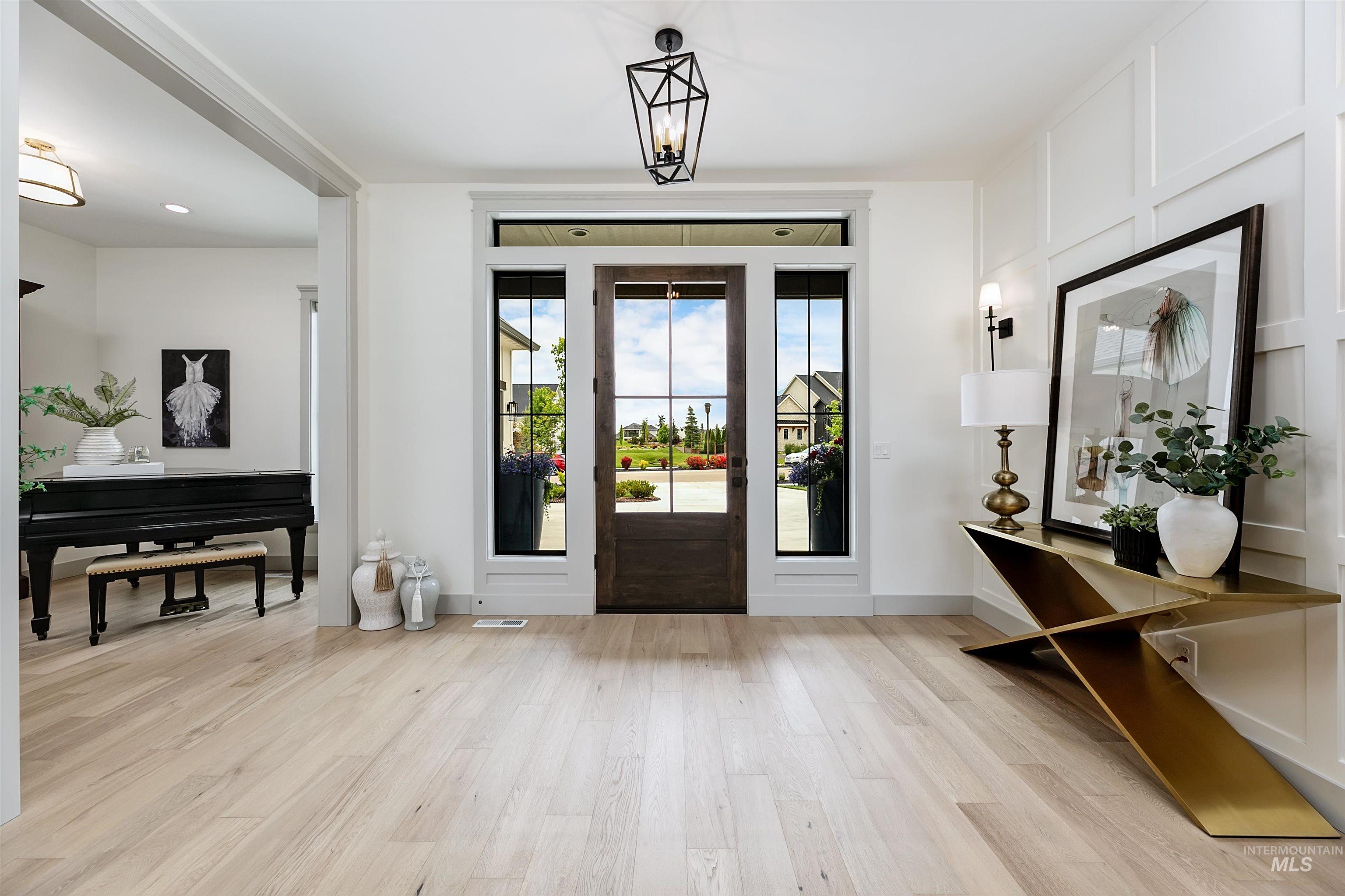 Spacious entryway featuring light wood-finish flooring, a dark wood-paneled door with sidelight windows, and a geometric pendant light fixture