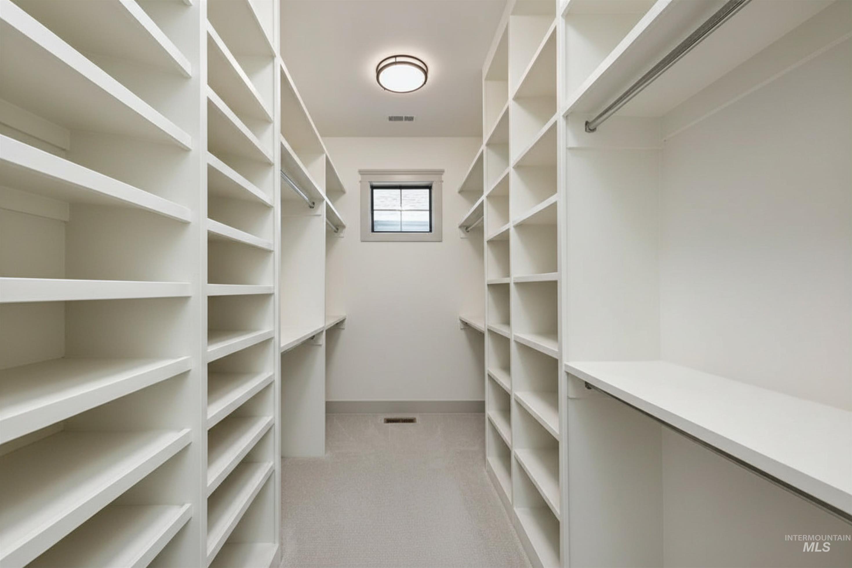 Spacious walk-in closet featuring extensive built-in shelving, hanging rods, and a neutral carpeted floor